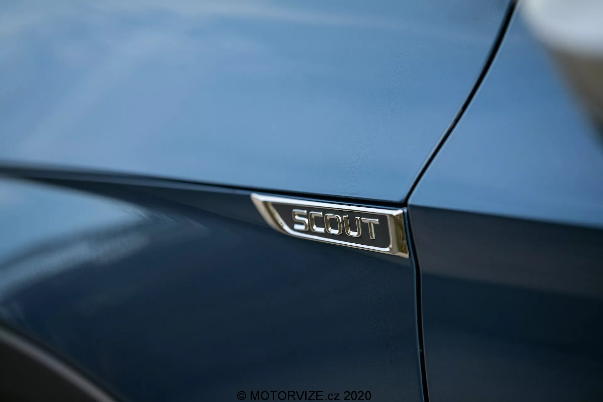 Close-up do emblema SCOUT em um Škoda Octavia 2020 azul escuro, mostrando a edição especial do carro com letras prateadas em um fundo preto, refletindo os detalhes luxuosos e o acabamento polido da pintura.
