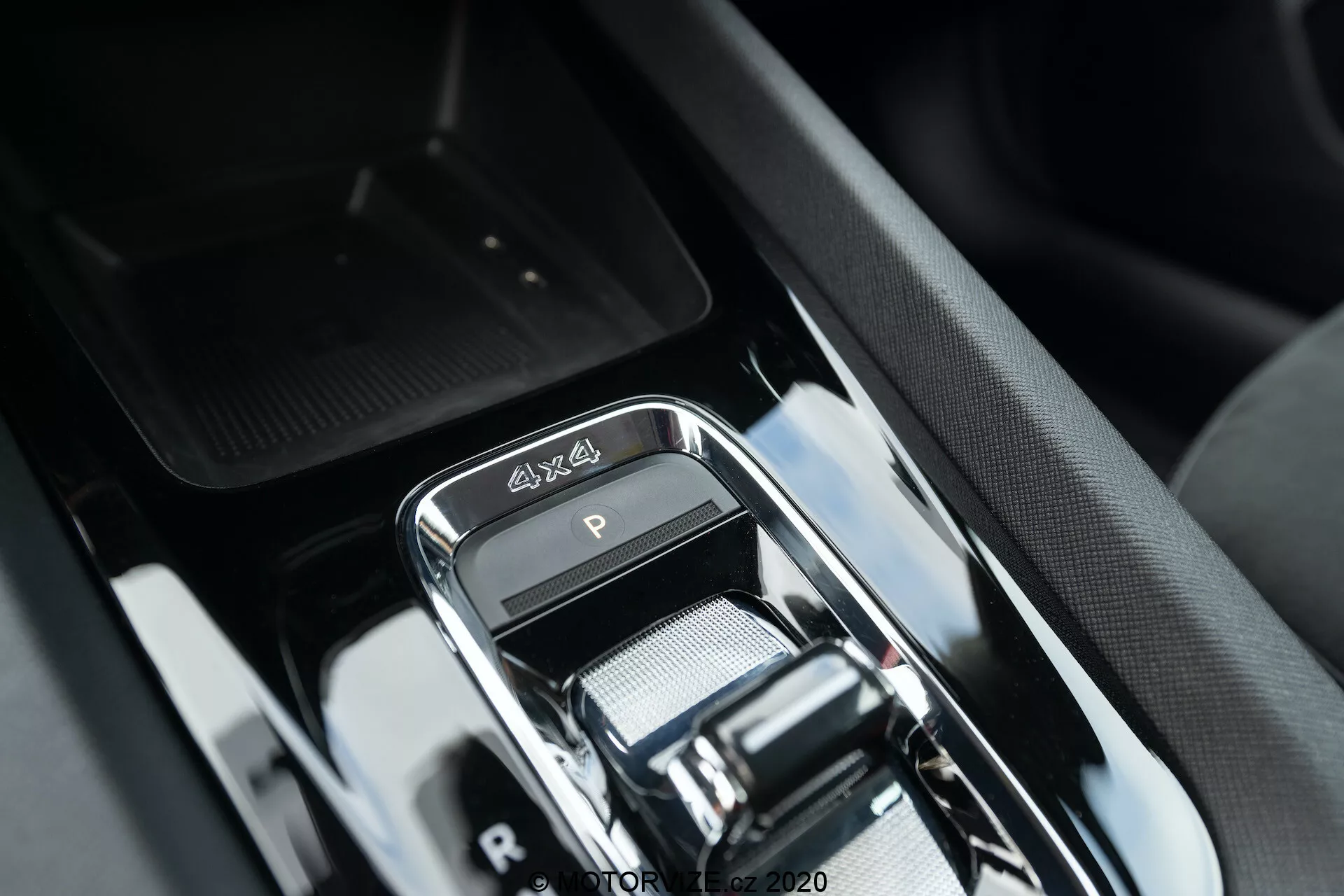 Close-up da área da alavanca de câmbio no luxuoso interior do Skoda Octavia Scout 2020, exibindo um seletor de marcha eletrônico moderno com acabamento cromado, emblema 4x4, elegante acabamento preto brilhante e design sofisticado do console central com botões circundantes e compartimento de armazenamento sugerido.