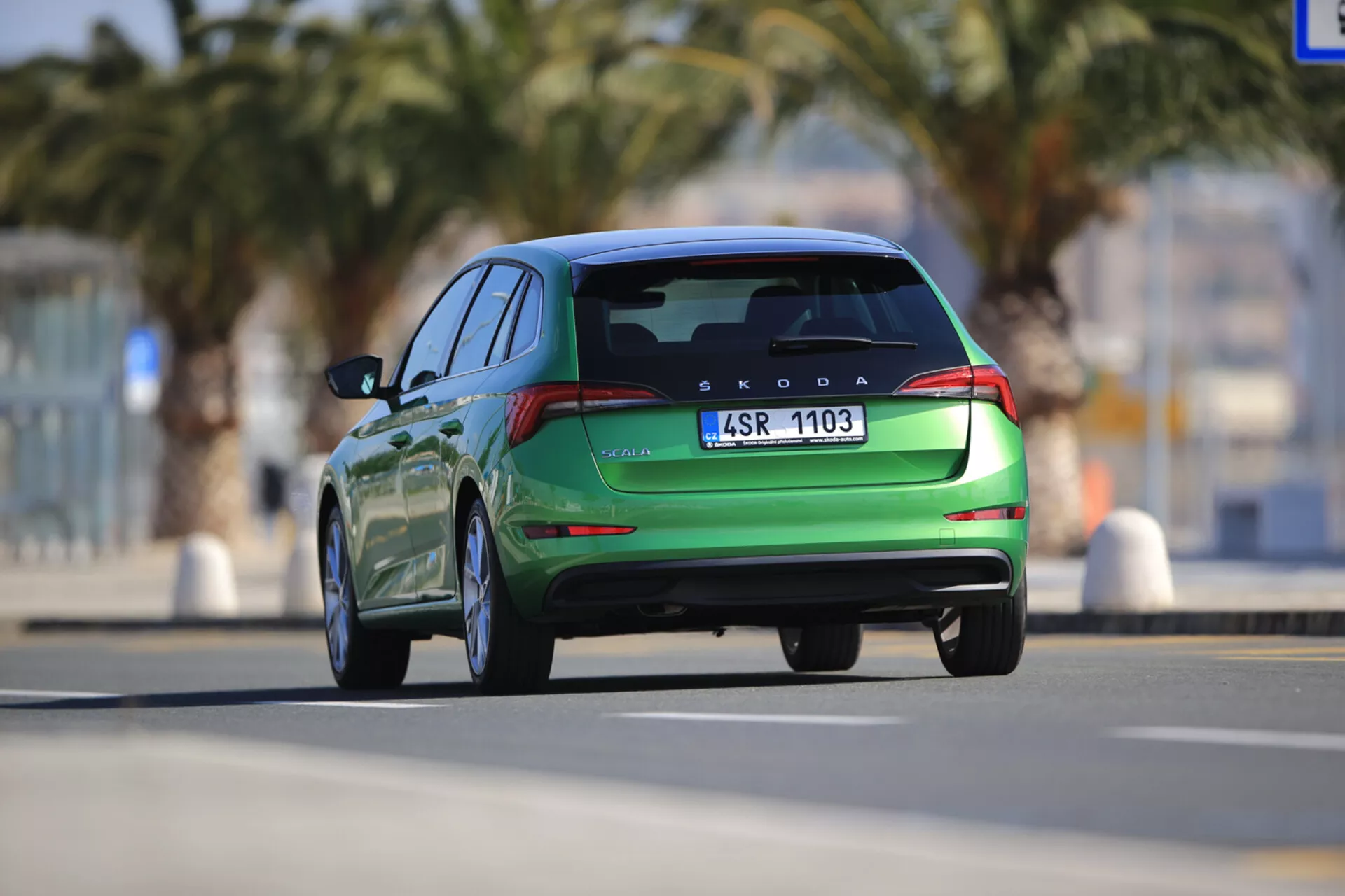 Vista traseira de um Skoda Scala verde 2019 em movimento, exibindo linhas de design, faróis traseiros LED, dupla saída de escape e sensores de estacionamento traseiros, capturada de um ângulo baixo com pouca profundidade de campo