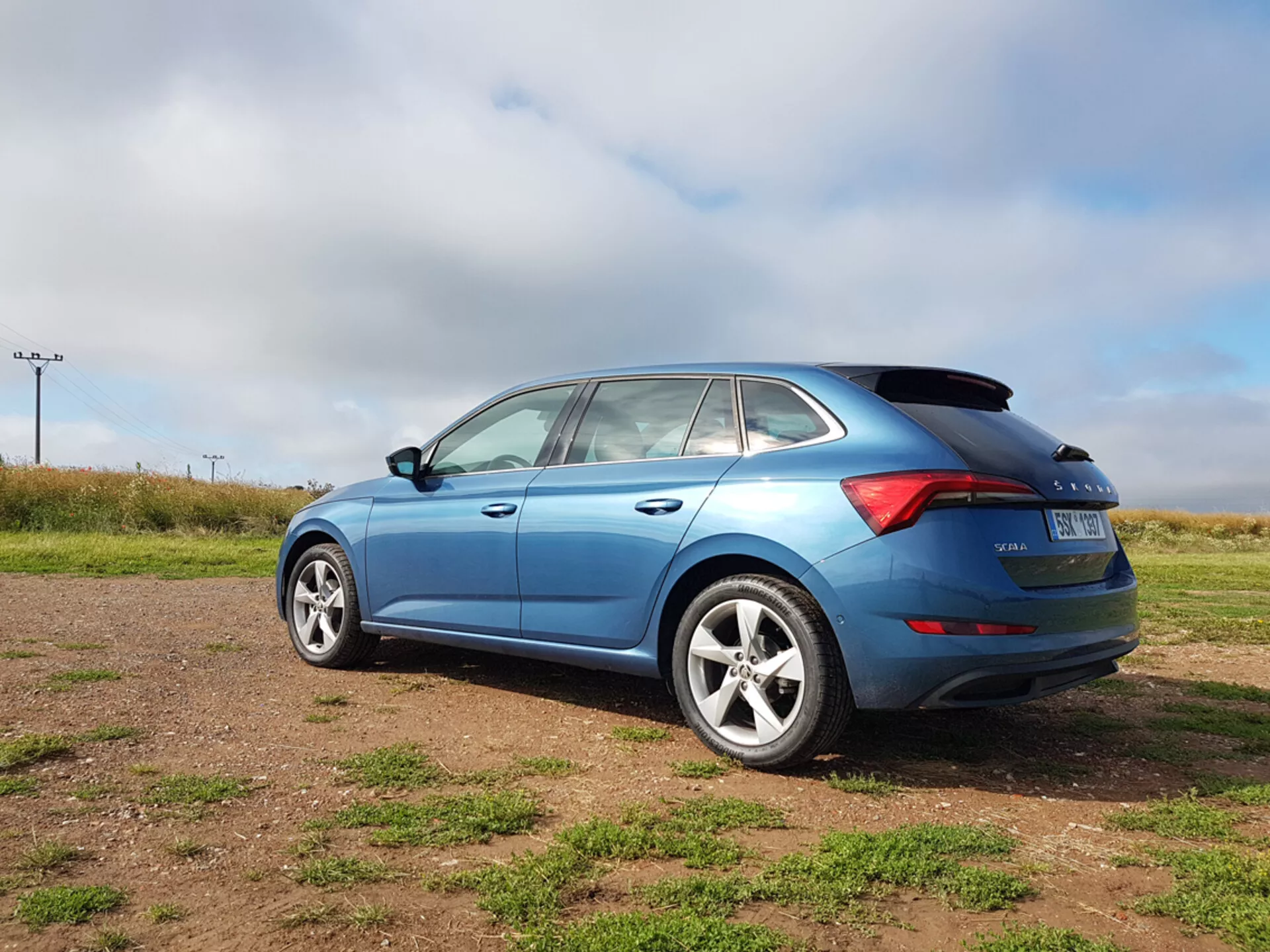 Hatchback azul Skoda Scala 2019 mostrando elementos de design lateral e traseiro, incluindo forma das janelas, luzes traseiras LED e rodas de liga leve, fotografado de um ângulo traseiro de três quartos em terreno gramado