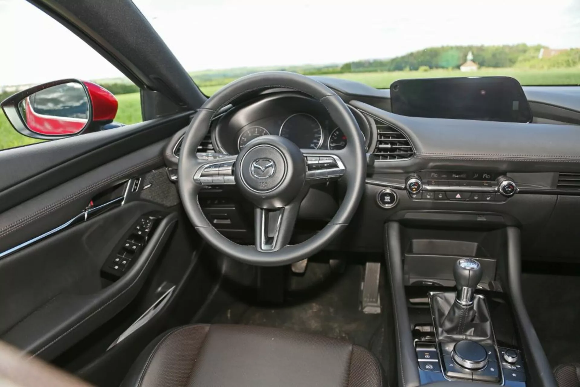 Vista interior do Skoda Scala 2019 focando no lado do motorista com assento do passageiro em couro, alavanca de transmissão manual, painel elegante com sistema de infotainment e volante multifuncional