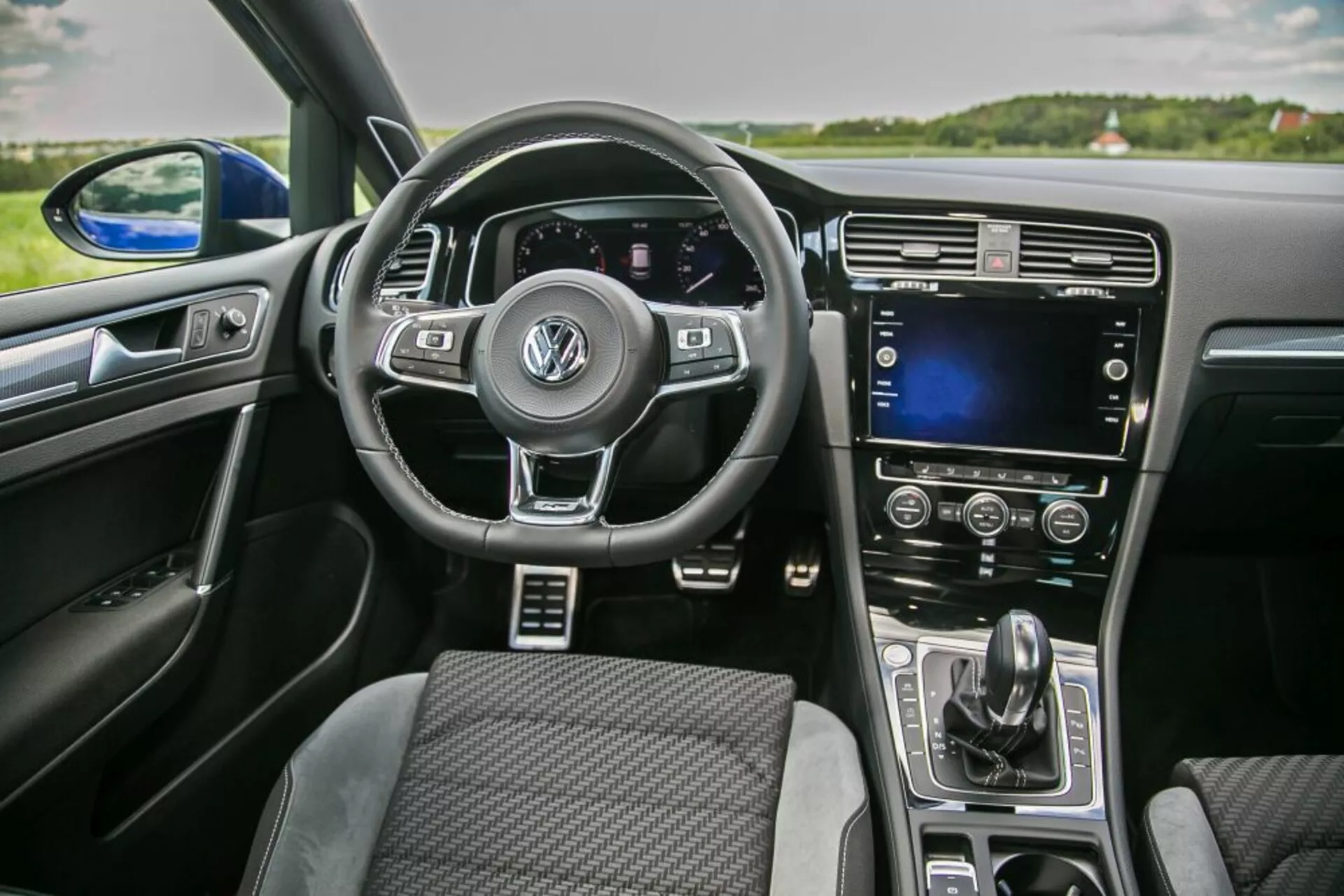 Vista interior de um Skoda Scala 2019 a partir da perspectiva do passageiro da frente apresentando um volante multifunções com logotipo Volkswagen, painel de instrumentos digital, ecrã tátil na consola central e controlo automático do clima