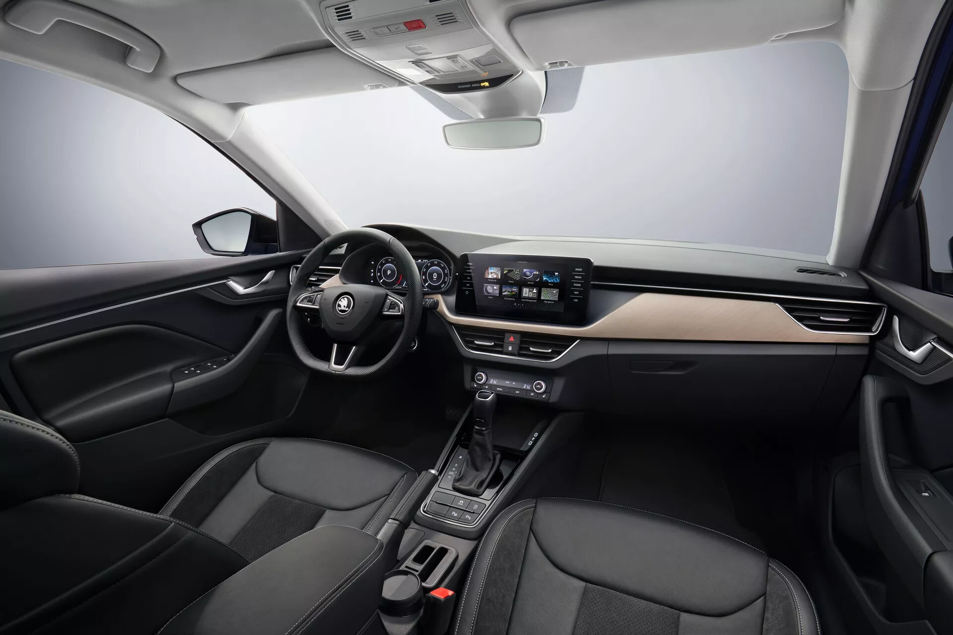 Interior do Skoda Scala 2019 exibindo o design moderno do cockpit com detalhes em metal escovado, sistema de infotainment central touchscreen, controles climáticos minimalistas e assentos dianteiros estofados em couro, visto de um ângulo frontal central.