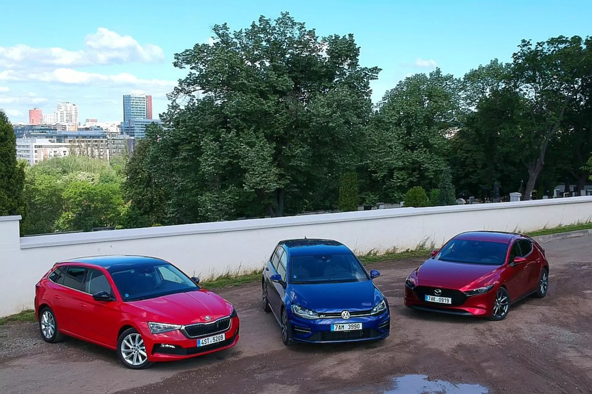 Hatchbacks Skoda Scala de 2019 estacionados lado a lado em um ambiente urbano, exibindo cores vermelho, azul e bordô com uma tomada de ângulo alto de uma posição elevada, destacando suas rodas de liga, faróis de halogênio e designs aerodinâmicos