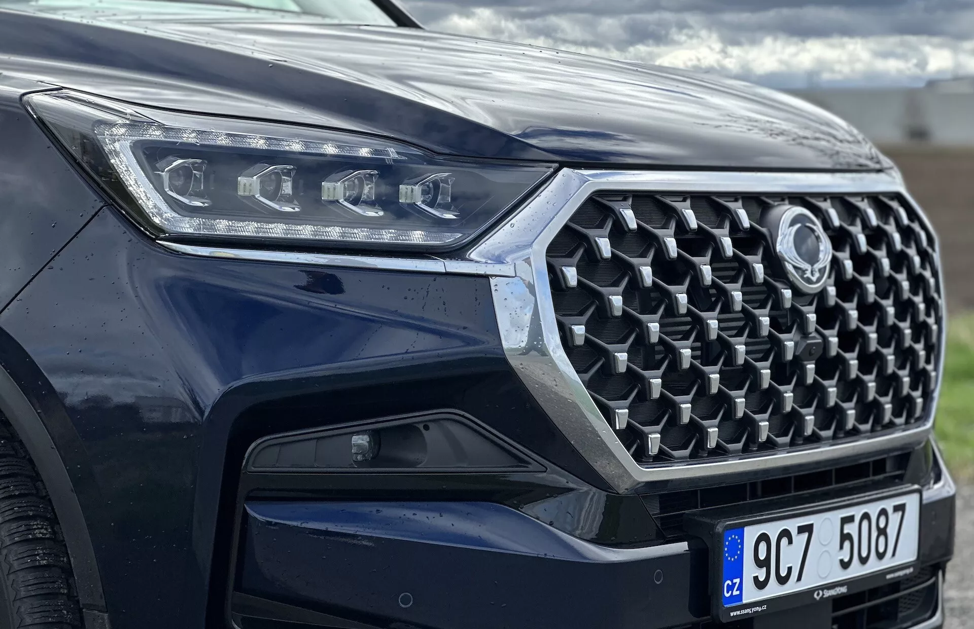 Vista frontal em ângulo do SsangYong Rexton 2021 focada na grade, para-choque dianteiro e design dos faróis LED, exibindo recursos de segurança avançados e tecnologia moderna com pintura metálica.