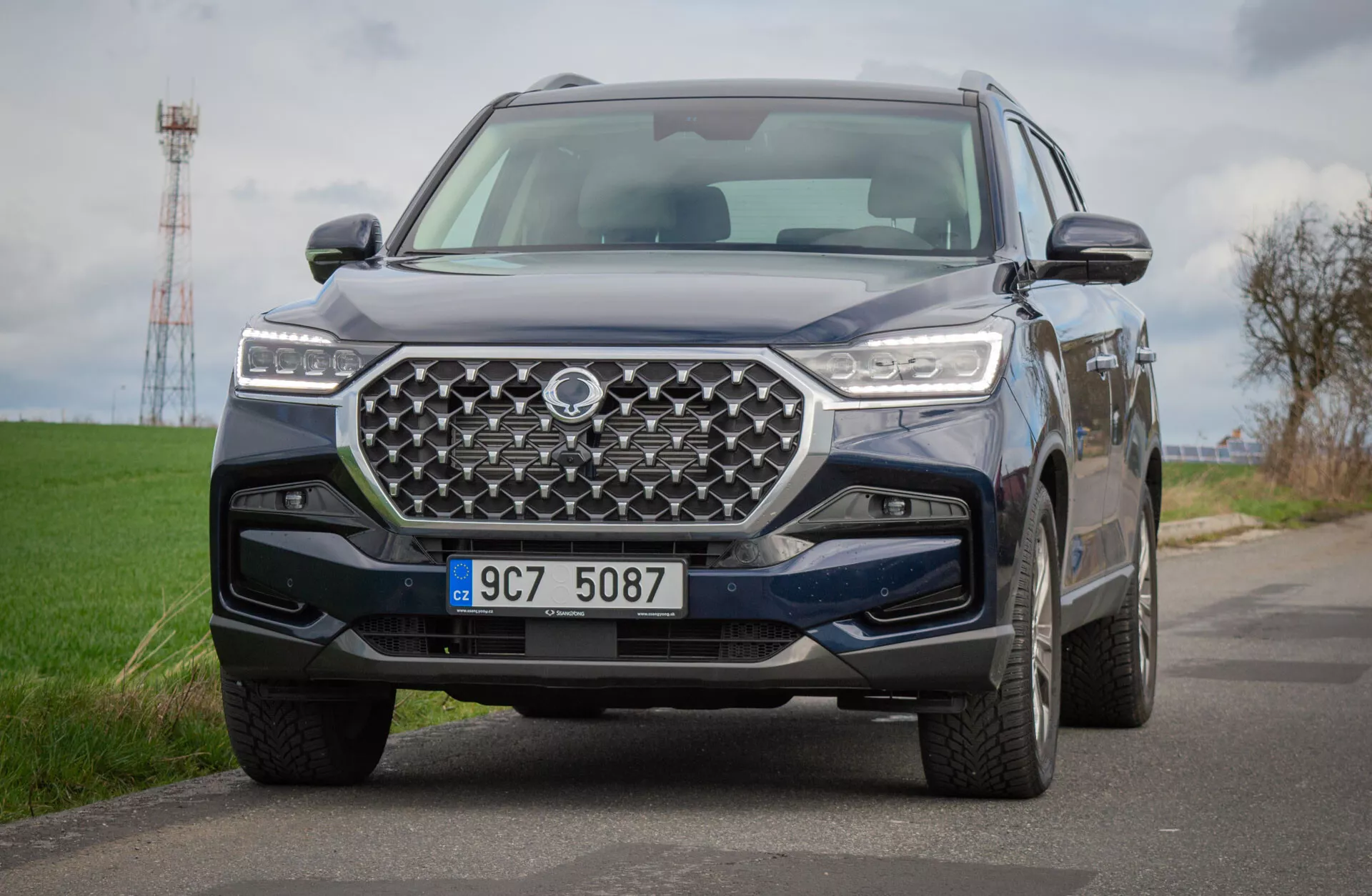 SUV SsangYong Rexton 2021 em estrada rural, exibindo uma vista detalhada de seu design frontal com grade geométrica e faróis LED, refletindo tecnologia avançada e capacidades off-road