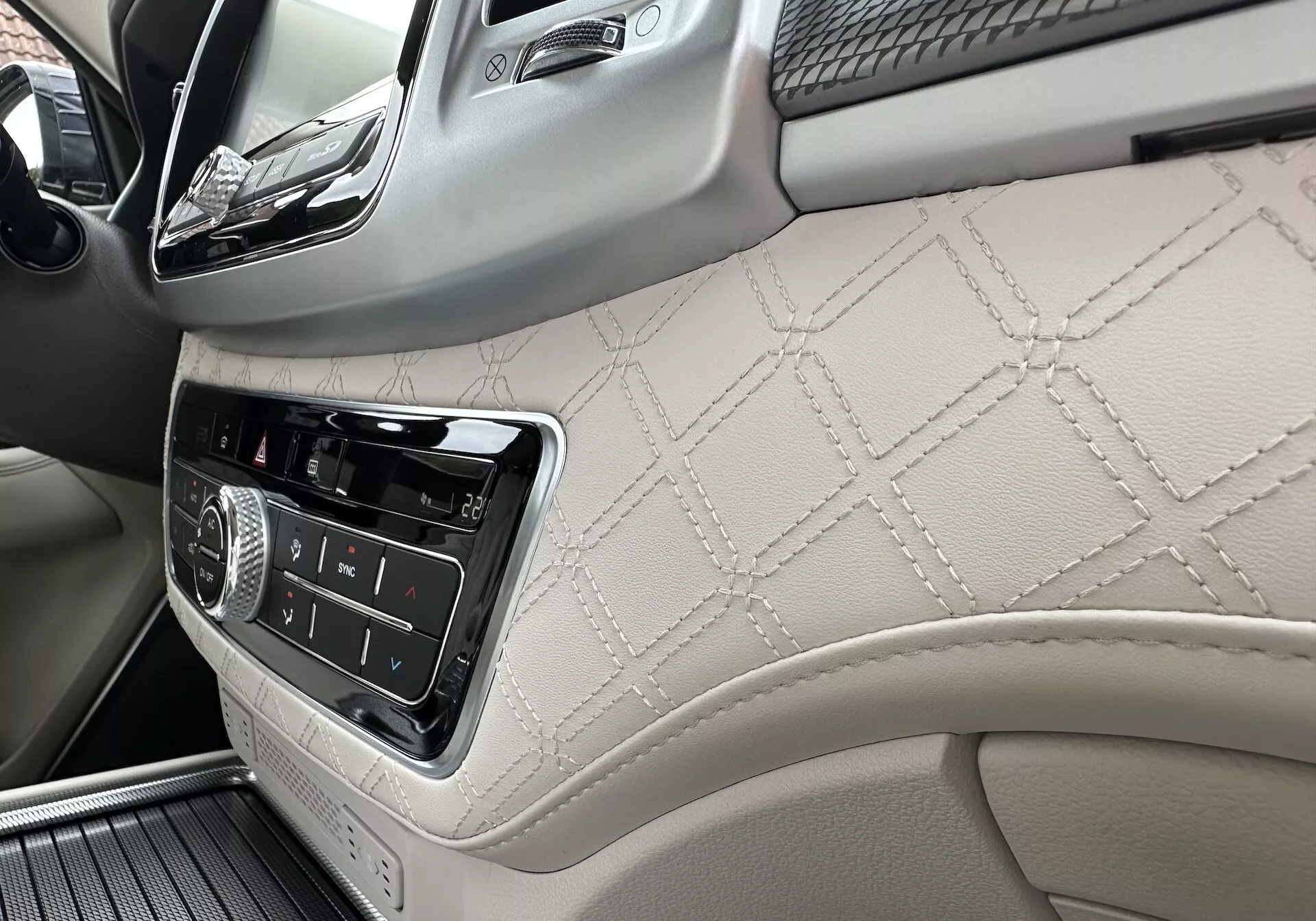 Interior do SsangYong Rexton 2021 focando no painel do lado do passageiro e parte do painel da porta frontal com couro costurado em formato de diamante, controles de infotenimento e detalhes de acabamento em madeira de luxo