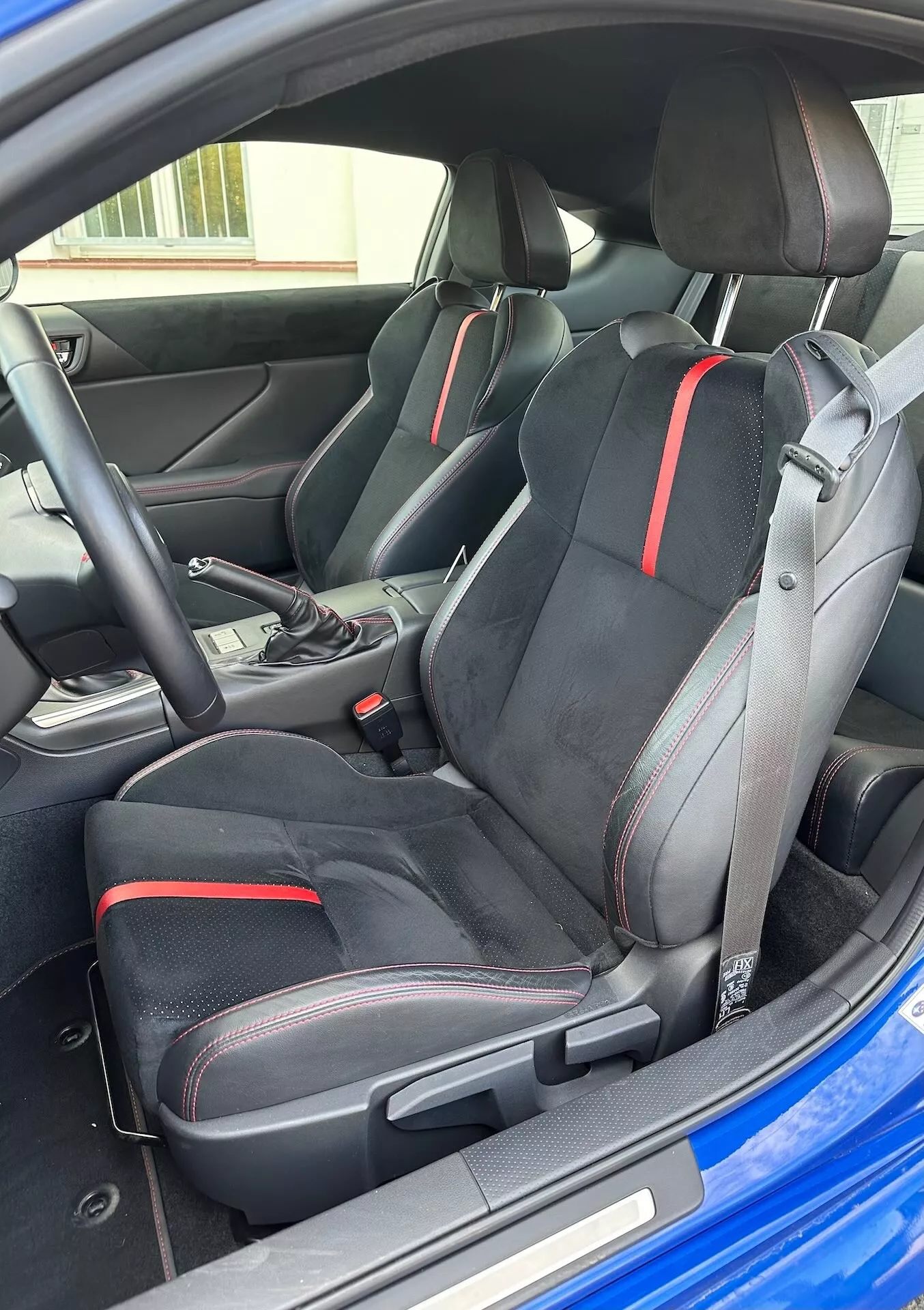 Vista interior do Subaru BRZ 2023 destacando os assentos dianteiros esportivos com design ergonômico e detalhes em vermelho, seletor de transmissão automática e estética moderna do cockpit a partir de uma perspectiva exterior oblíqua