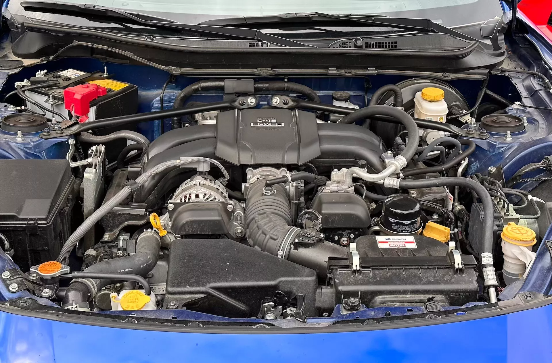 Vista detalhada do compartimento do motor da Subaru BRZ 2023 com motor BOXER, bateria, reservatórios de fluido e sistema de admissão de ar visíveis