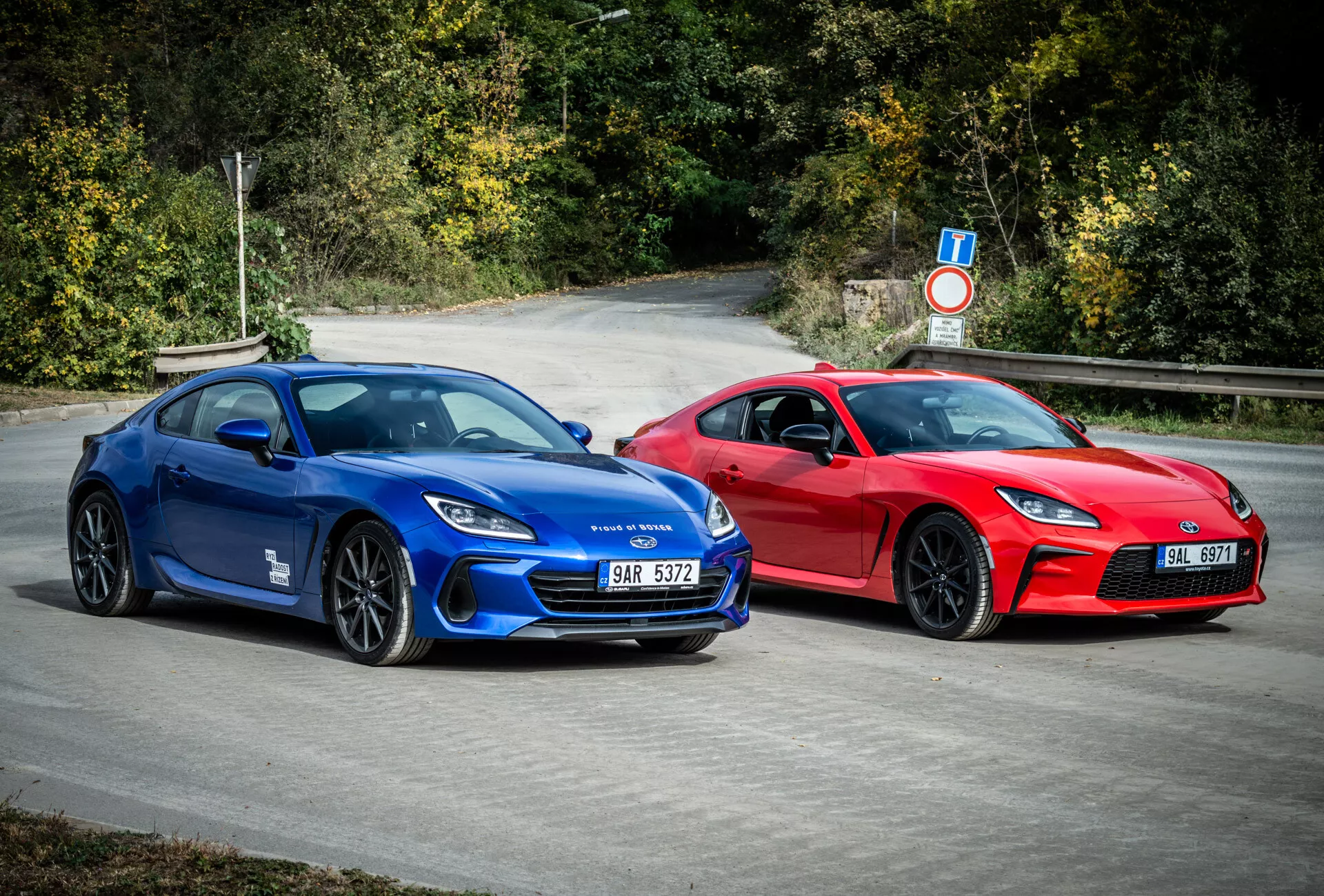 Coupés esportivos Subaru BRZ 2023 em azul e vermelho com design aerodinâmico e recursos de performance, estacionados ao ar livre rodeados por folhagem natural
