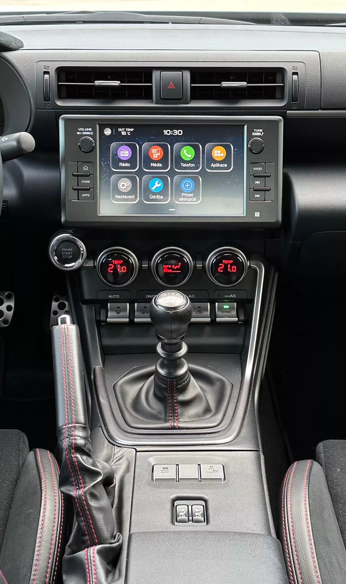 Interior do Subaru BRZ 2023 mostrando o console central, com tela de toque para infotainment, indicador de luz de perigo, saídas de ar metálicas, controle de clima de duas zonas, manopla de câmbio manual com revestimento de couro, controles do aquecedor de assentos e um seletor de modo de condução múltiplo em um design moderno preto e metálico.