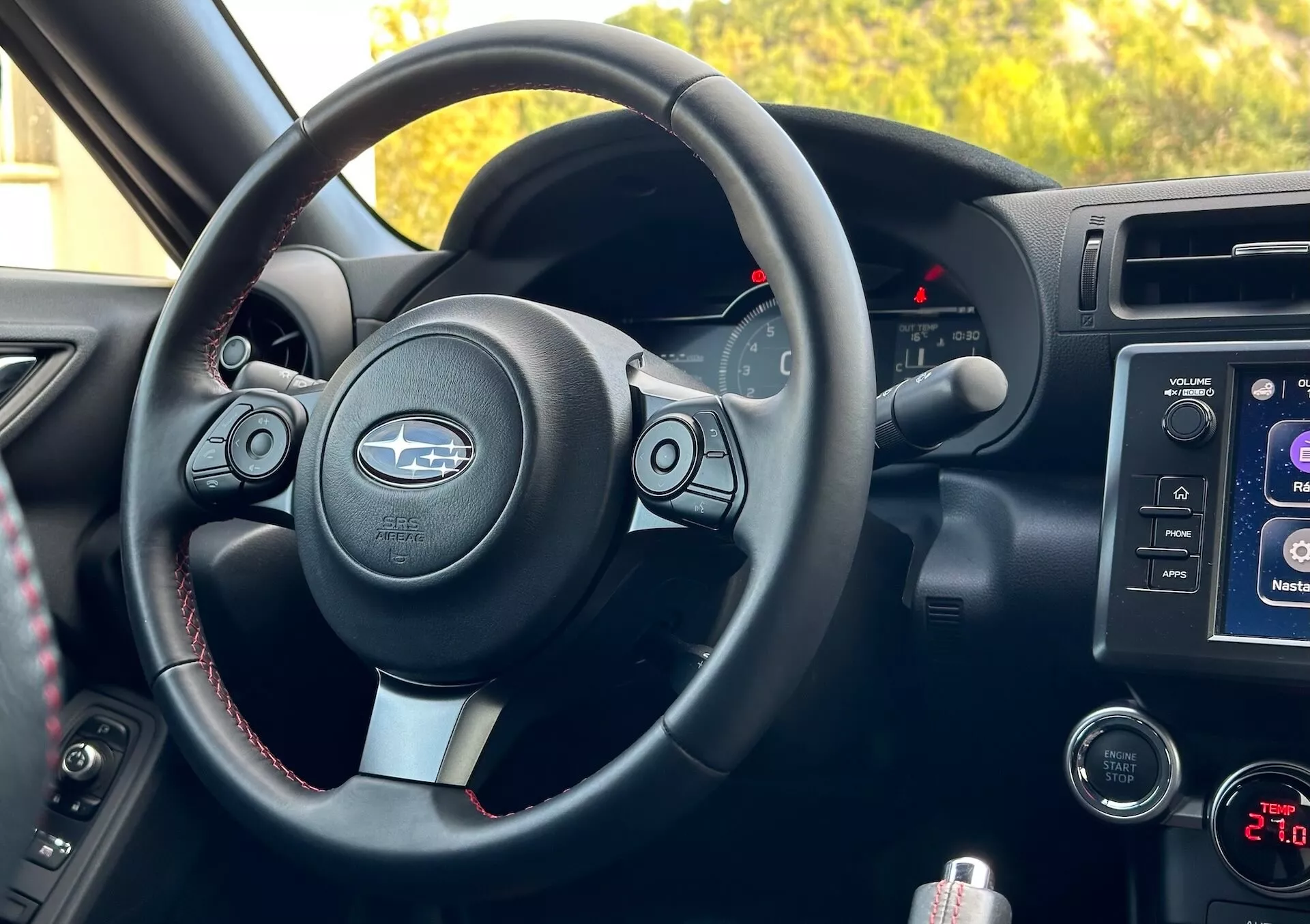 Vista interior do Subaru BRZ 2023 pela perspectiva do passageiro mostrando o volante com acentos metálicos e logotipo Subaru, botões de controle, costura contrastante, cluster de instrumentos com indicadores retroiluminados, sistema de infotainment no console central, controles de áudio e clima, e compartimento de armazenamento.