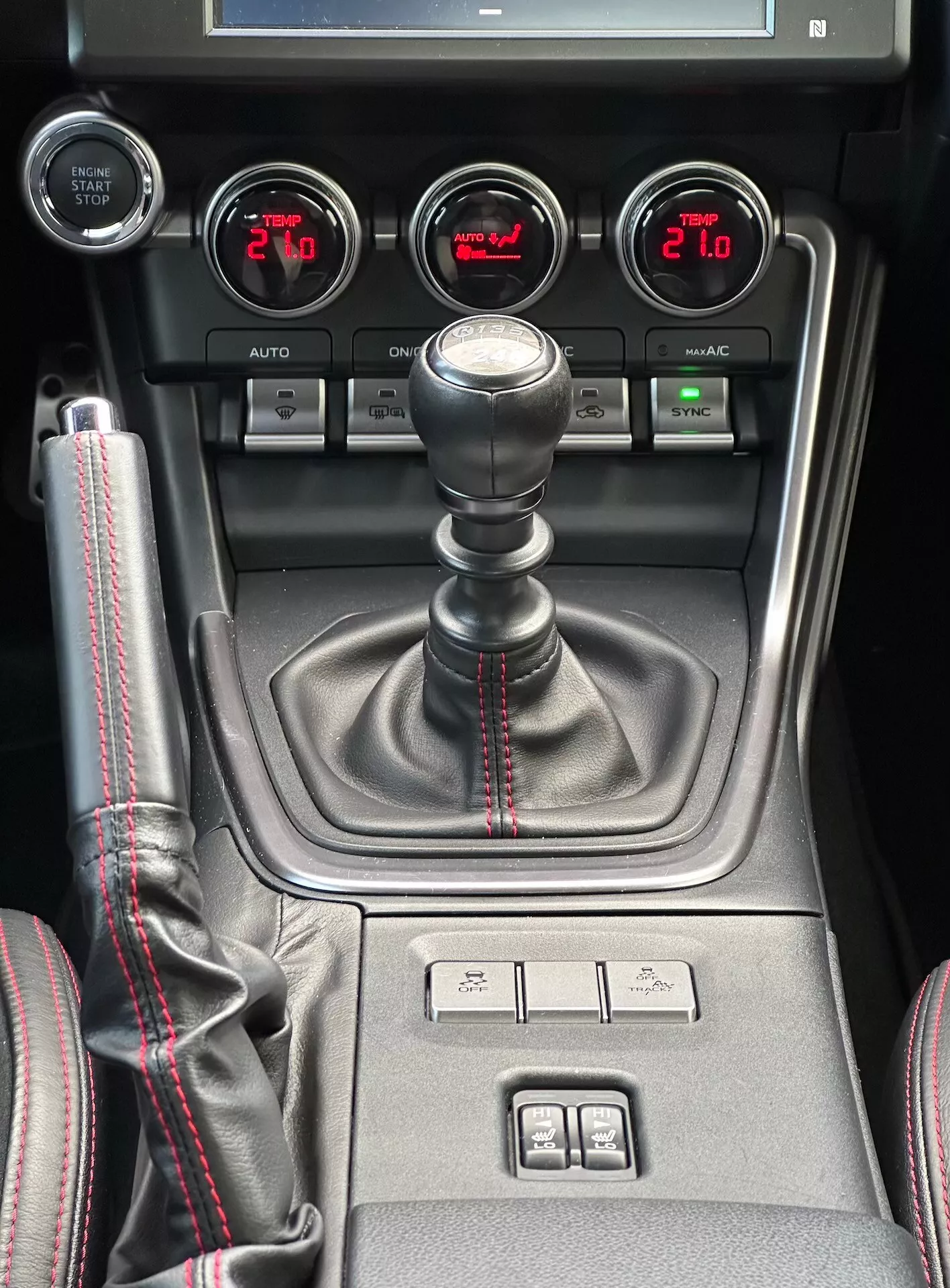 Console central do Subaru BRZ 2023 com alavanca de transmissão manual com costura vermelha esportiva, medidores auxiliares para pressão do turbo, voltagem da bateria, temperatura do óleo e controle de clima de zona dupla em vista detalhada do interior