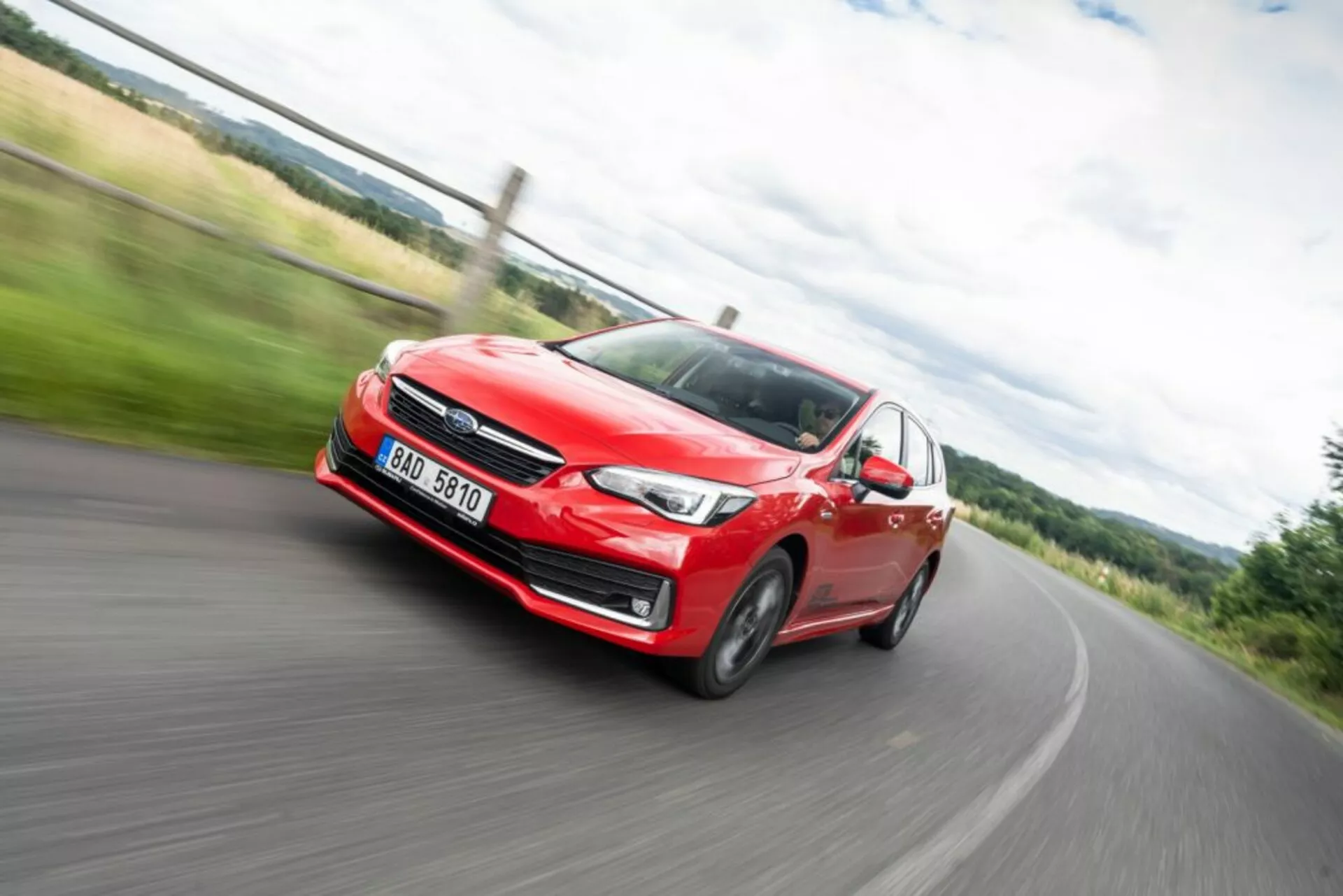 Imagem dinâmica com desfoque de movimento de um Subaru Impreza vermelho de 2018 em ação, vista frontal mostrando farol, grade e rodas de liga durante uma curva à esquerda em uma estrada rural
