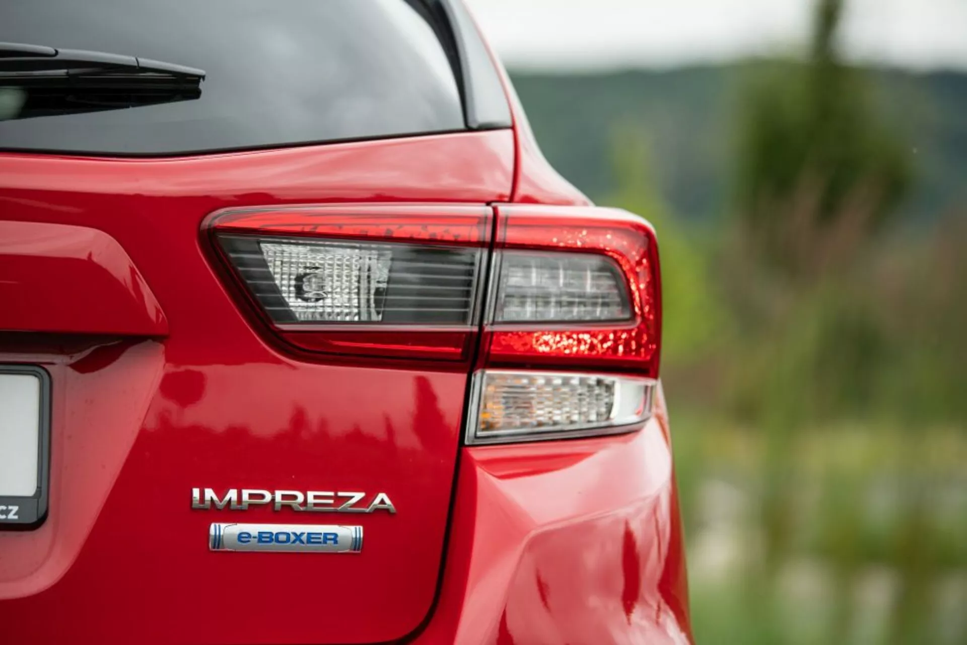 Close-up do canto traseiro de um Subaru Impreza vermelho de 2018, focando na luz traseira e no emblema do motor híbrido 'e-BOXER', destacando a tecnologia híbrida avançada e a iluminação LED da Subaru