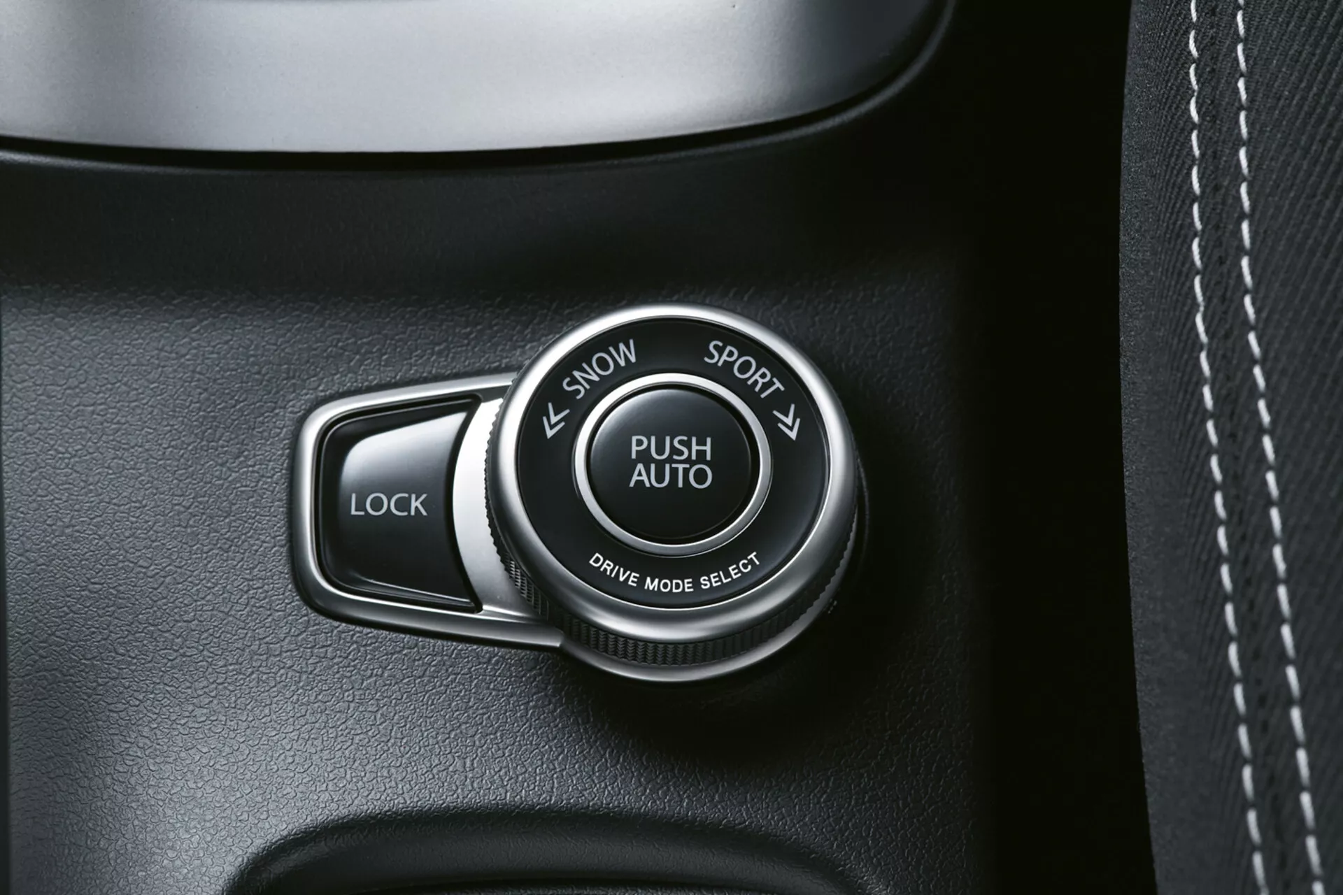 Visão detalhada do interior do Suzuki S-Cross 2022 mostrando o seletor de modo de condução rotulado 'PUSH AUTO' com opções 'SNOW' e 'SPORT', ao lado de um botão 'LOCK', em um painel de alta qualidade de tons escuros, possivelmente texturizado como couro com costura visível.
