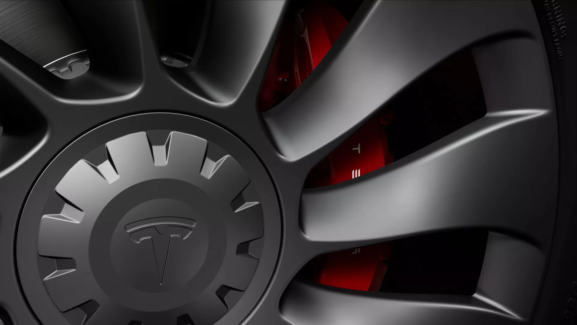 Uma vista de close-up da roda de um Tesla Model-3 2019 (1ª Geração), mostrando uma roda multi-raios de alto desempenho com um acabamento fosco escuro, indicativo de uma estética esportiva ou premium. O design intrincado em forma de turbina auxilia na refrigeração dos freios e na aerodinâmica. A tampa central está intencionalmente obscurecida para ocultar a marca. Atrás dos raios, uma pinça de freio vermelha é parcialmente visível, sinalizando um sistema de freios orientado para desempenho. O disco de freio ventilado, projetado para dissipar o calor de forma eficiente, espreita e a borda do pneu de perfil baixo é quase invisível. A iluminação dramática realça a textura e a forma, destacando a capacidade tecnológica dos componentes da roda e do freio.