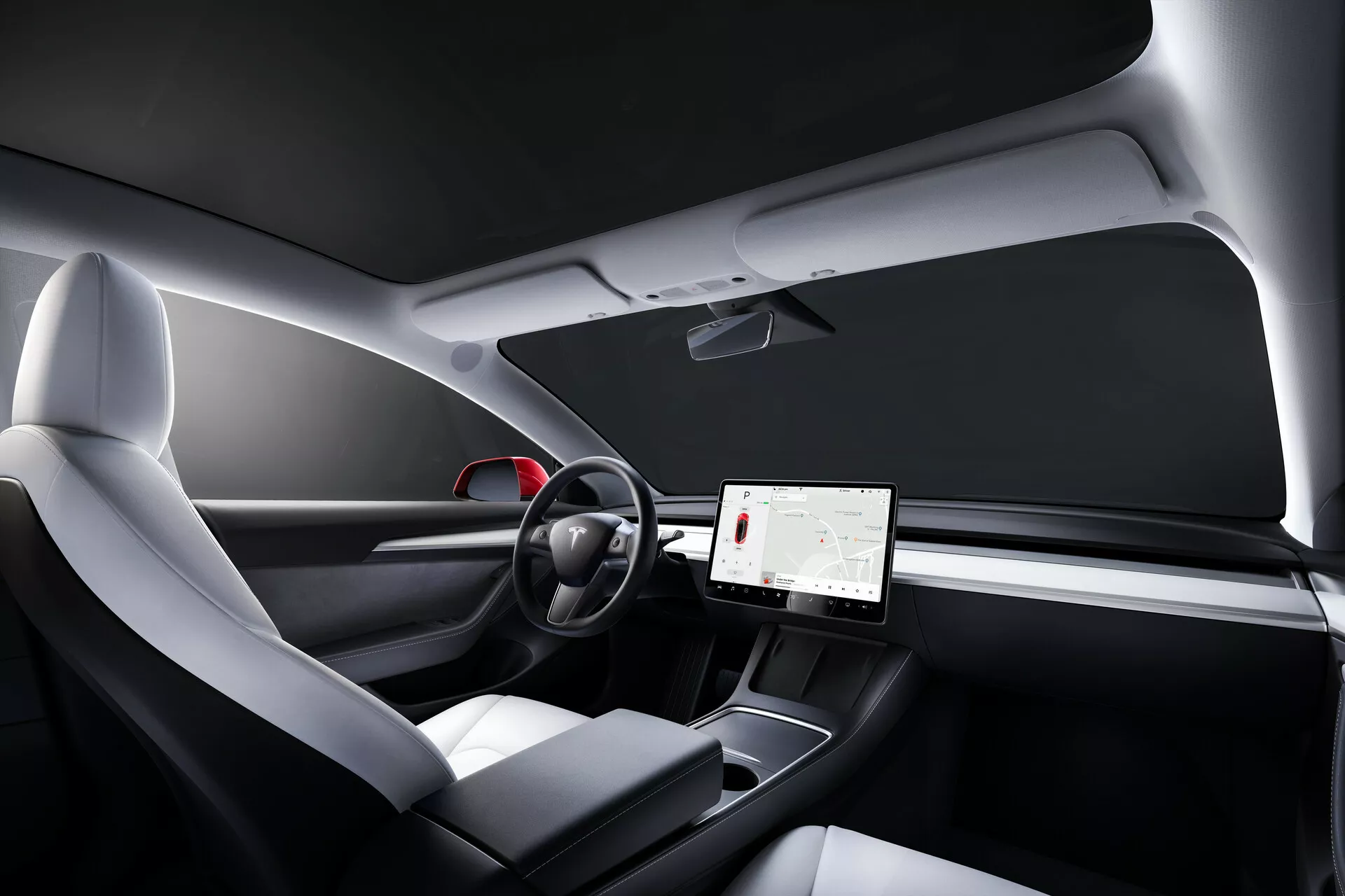 Foto do interior do Tesla Model 3 2019 (1ª geração) a partir da perspetiva do passageiro, mostrando um design minimalista do painel de instrumentos, um grande ecrã tátil central, um volante de duas hastes com controlos táteis, assentos ergonómicos modernos com estofos de materiais mistos, uma consola central elegante, toques decorativos semelhantes a madeira e um teto panorâmico de vidro.