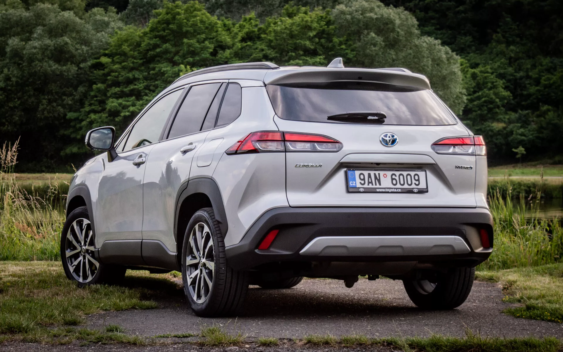 Vista traseira de três quartos do Toyota Corolla Cross 2022 mostrando luzes traseiras LED, emblema híbrido e sensores de assistência ao estacionamento