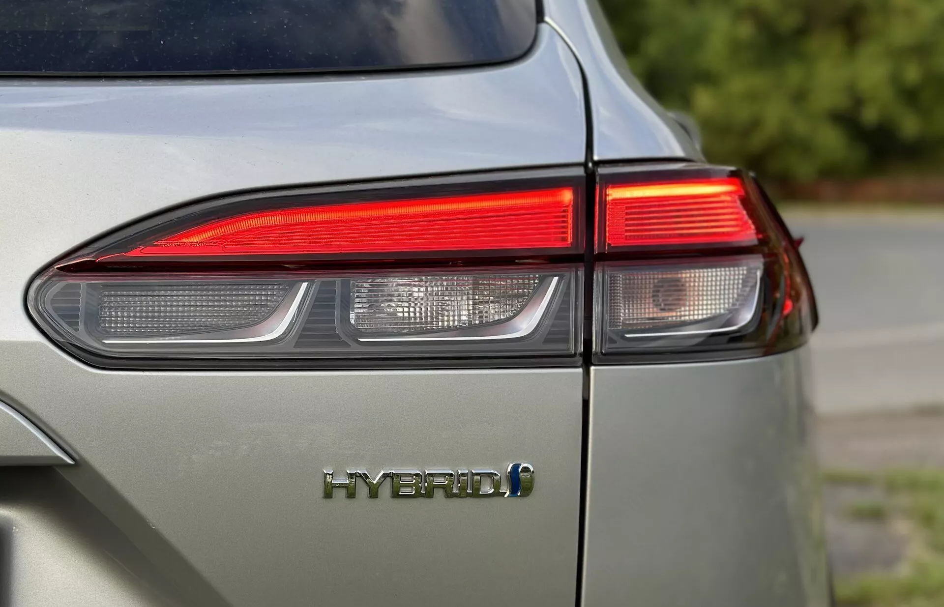 Close-up do canto traseiro esquerdo do Toyota Corolla-Cross 2022 mostrando o design da luz traseira LED e o emblema HYBRID com foco na tecnologia ambientalmente amigável do veículo e acabamento brilhante em uma cor cinza claro apagado