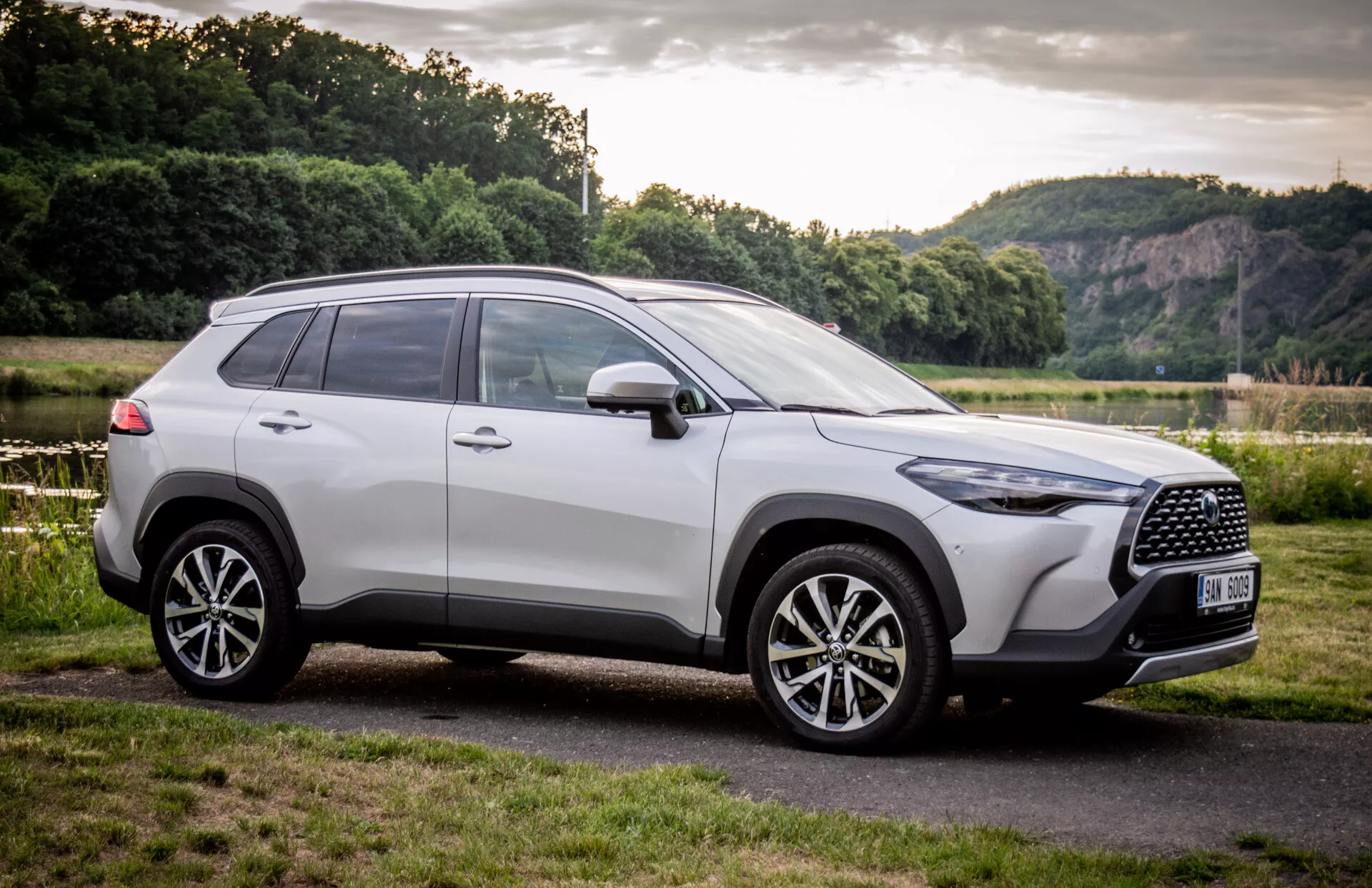 SUV Toyota Corolla Cross 2022 estacionado ao ar livre, mostrando seu design moderno de um ângulo frontal de três quartos com foco na grade, rodas de liga leve e perfil lateral contra um cenário natural