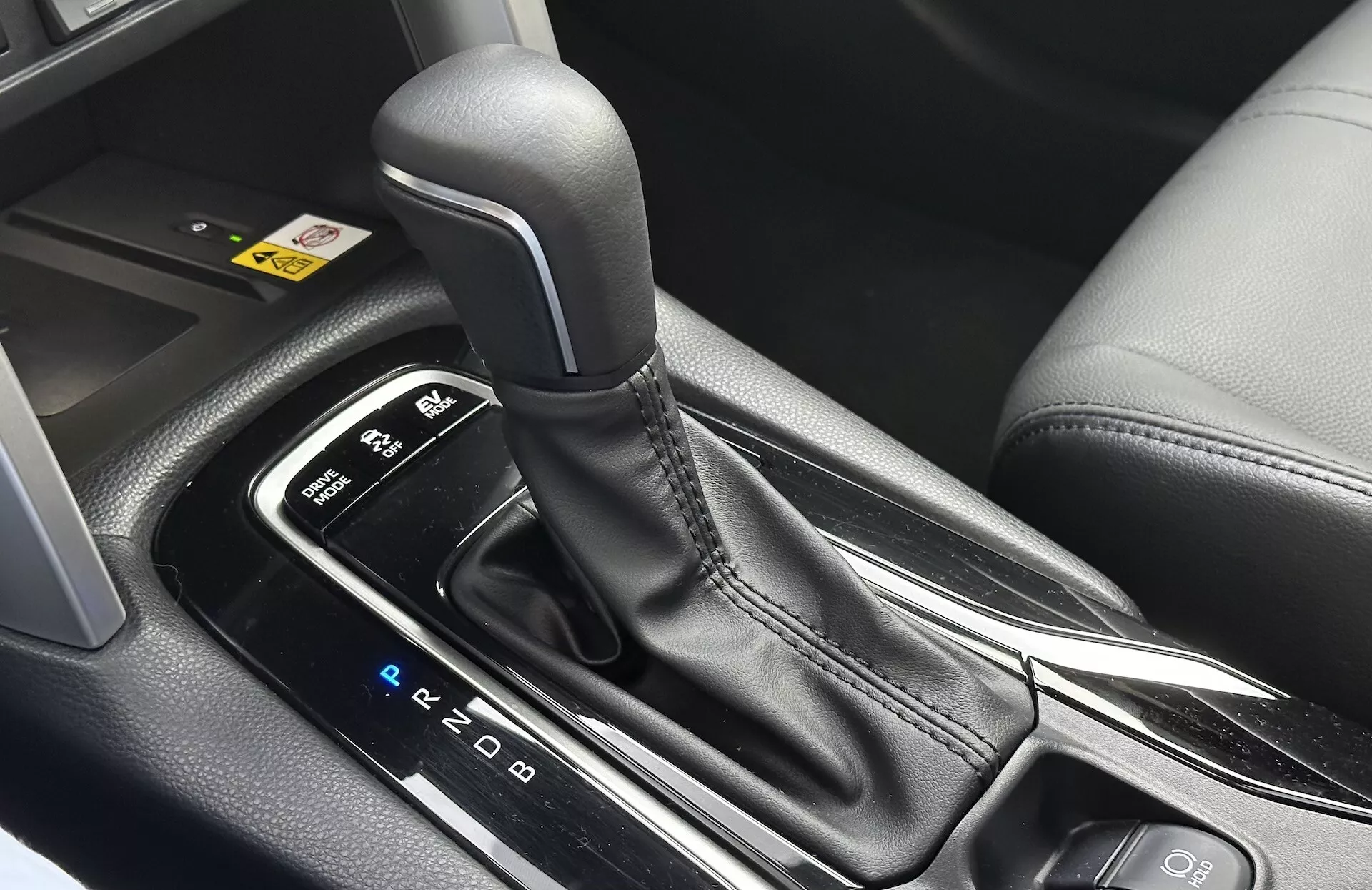 Vista detalhada do interior do Toyota Corolla Cross 2022 mostrando a alavanca de mudança de marchas automática com layout PRND visível, cercada por um console central elegante com acabamentos em plástico preto e detalhes metálicos, destacando o design ergonômico e as características tecnológicas modernas