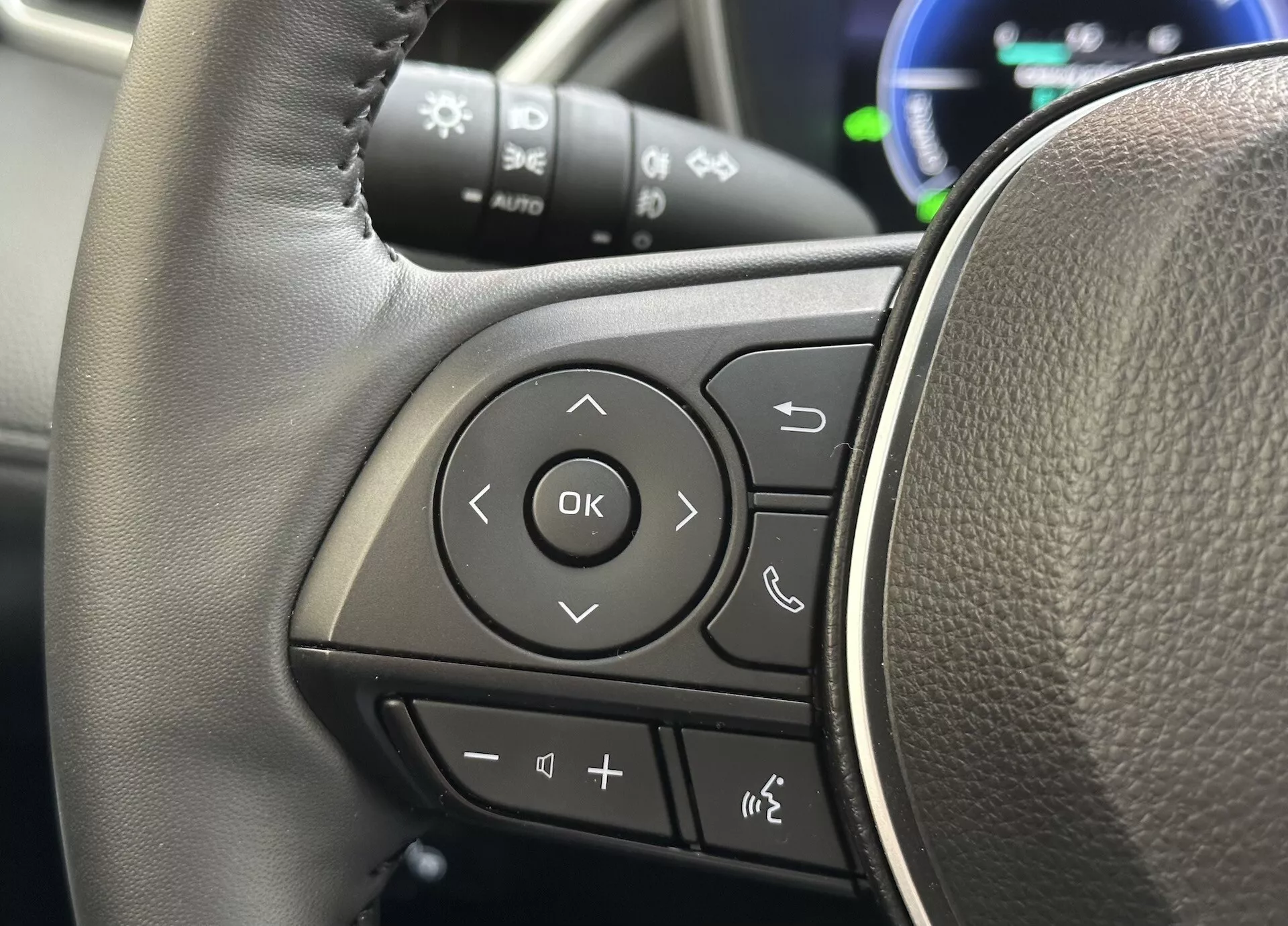 Vista detalhada do volante do Toyota Corolla Cross 2022 focando nos controles multifuncionais no raio esquerdo com textura semelhante à couro e botões claramente marcados para áudio, conectividade telefônica Bluetooth, comandos de voz e navegação pelo sistema de informação do motorista