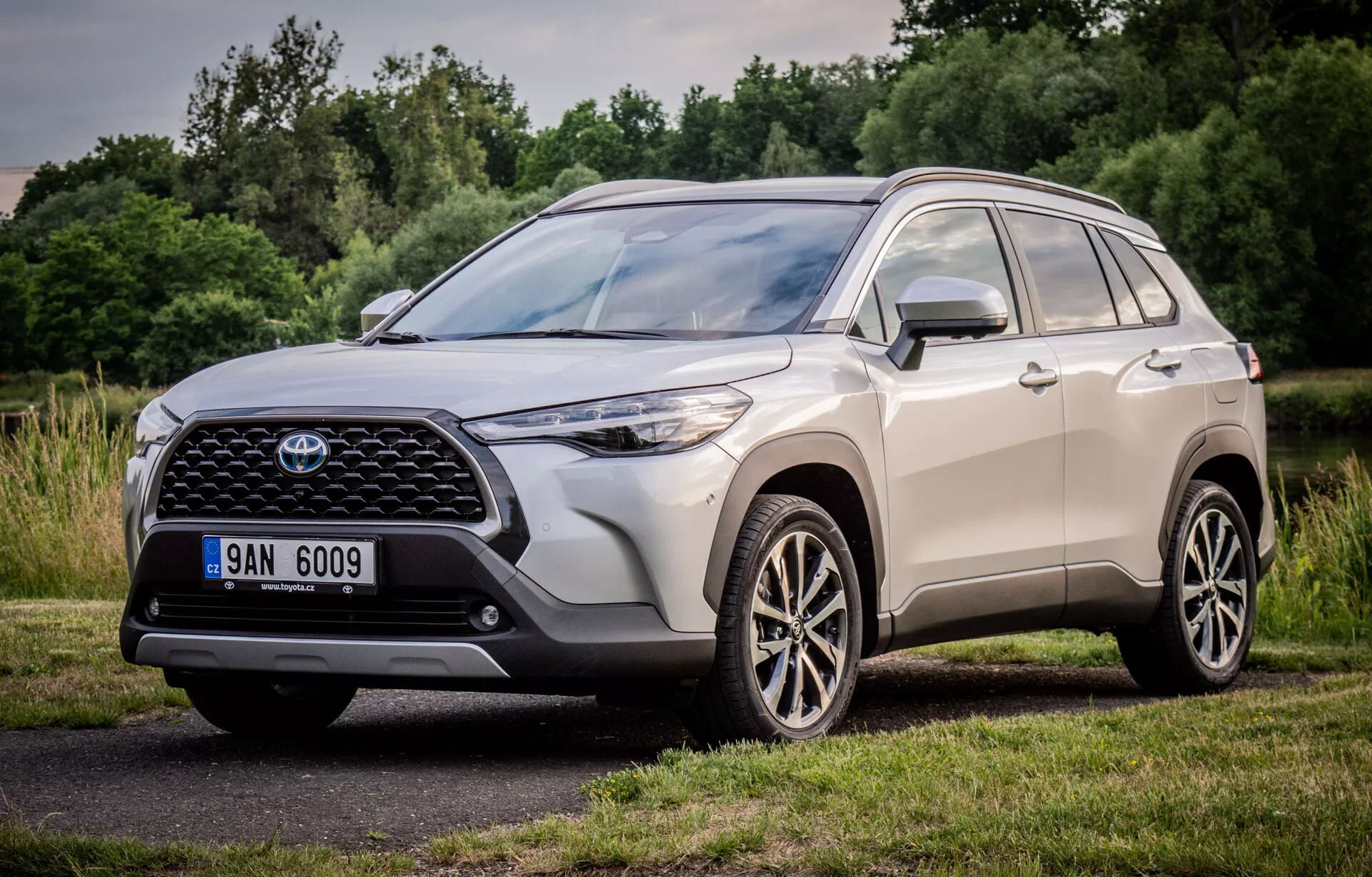 Toyota Corolla Cross 2022 exibindo seu design dinâmico com uma visão de perspectiva frontal de três quartos, destacando a grade frontal grande e padronizada, unidades de farol LED elegantes e rodas de liga leve multirradas, estacionado em um cenário natural
