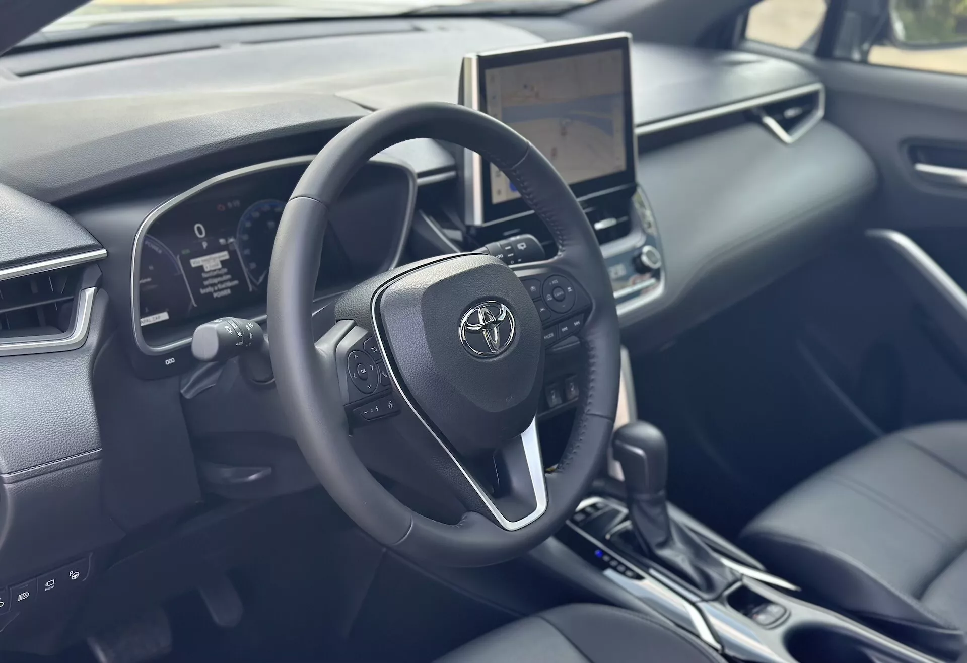 Interior do Toyota Corolla Cross 2022 focado no lado do motorista com volante detalhado, cluster de instrumentos digital, e tela tátil de infotainment central apresentando tecnologia moderna e acabamentos em couro preto