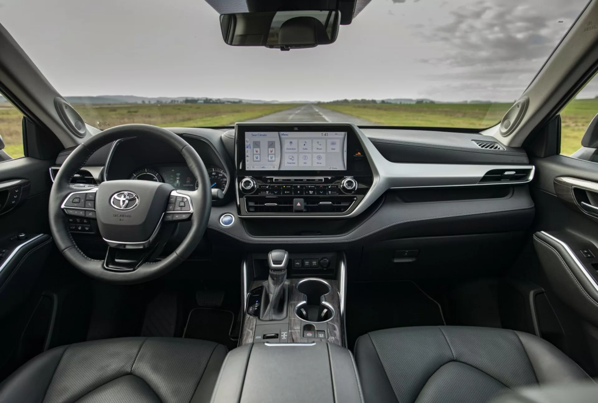 Visão geral do interior do Toyota Highlander 2021 mostrando painel de instrumentos, cluster de instrumentos digitais, display do sistema de infotenimento e assentos dianteiros revestidos em couro a partir da perspectiva dos assentos traseiros