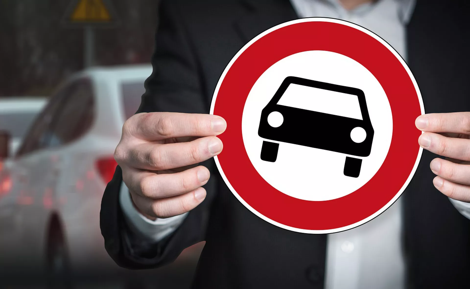 Indivíduo segurando uma placa circular vermelha com ícone de silhueta de carro branco, simbolizando a representação genérica de um automóvel contra um fundo urbano desfocado
