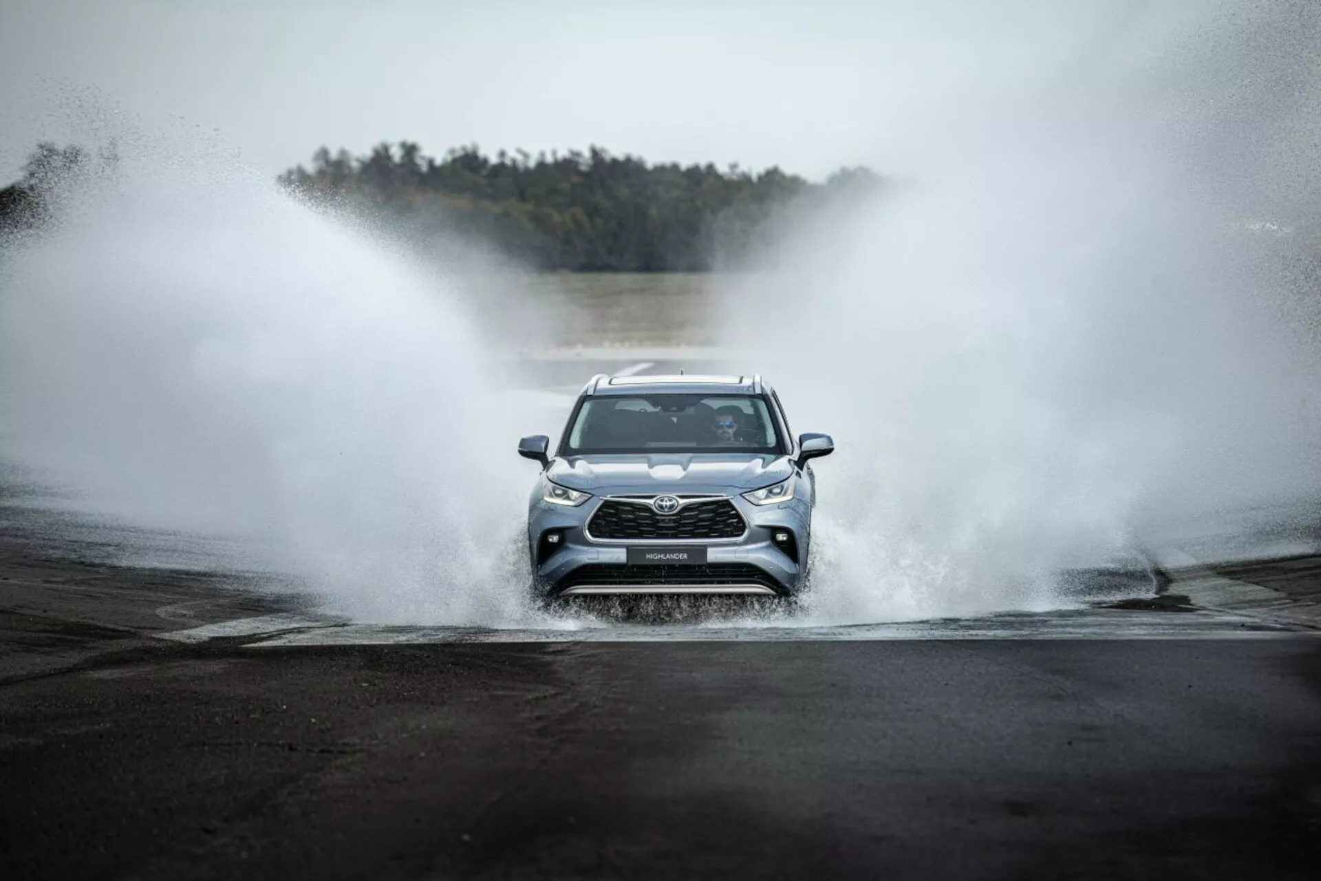 Toyota Highlander 2021 dirigindo de frente através da água, exibindo grade frontal, faróis LED e design esportivo em um cenário aventureiro