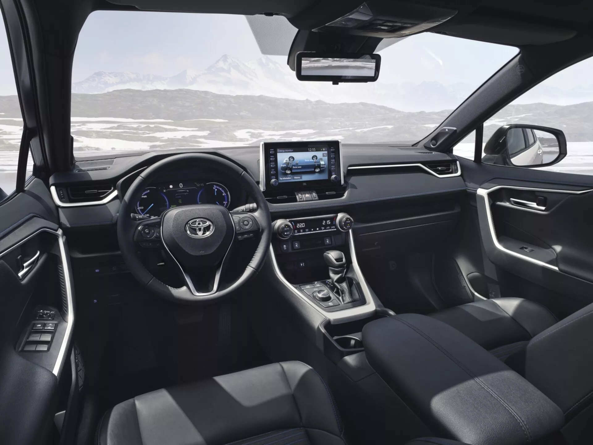 Vista interior do Toyota RAV4 2019 a partir do banco traseiro, destacando o design moderno e as características tecnológicas incluindo o volante com botões de controle, display digital, sistema de infotainment touchscreen, alavanca de câmbio automática, assentos estofados em escuro, e controles no painel da porta com uma paisagem montanhosa nevada visível através do para-brisa.