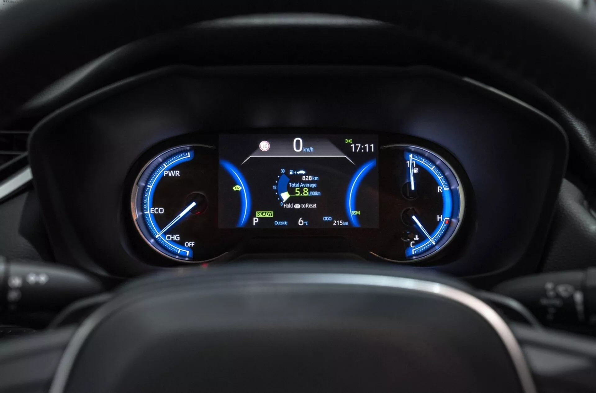Close-up do cluster de instrumentos do Toyota RAV4 2019 mostrando medidores híbridos com medidor de potência, velocímetro, e display digital central indicando posição estacionária, eficiência de combustível, e temperatura externa da perspectiva do motorista.