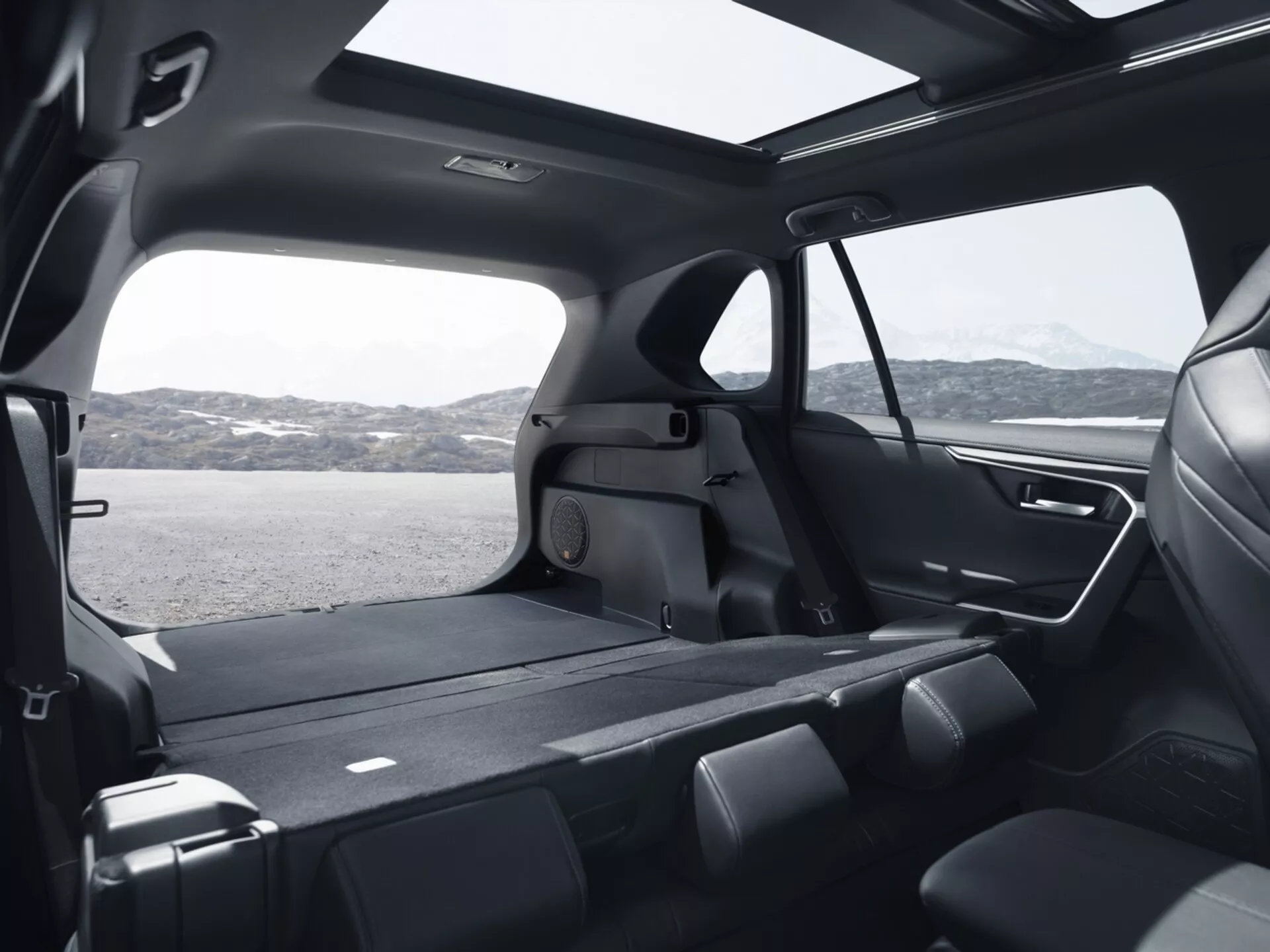 Vista interior de um Toyota RAV4 2019 mostrando a espaçosa cabine traseira de um ângulo alto, destacando os assentos dobráveis da segunda fila, amplo espaço de carga, grandes janelas com película, design moderno com materiais premium, teto solar panorâmico, sistema de iluminação avançado e recursos de controle climático