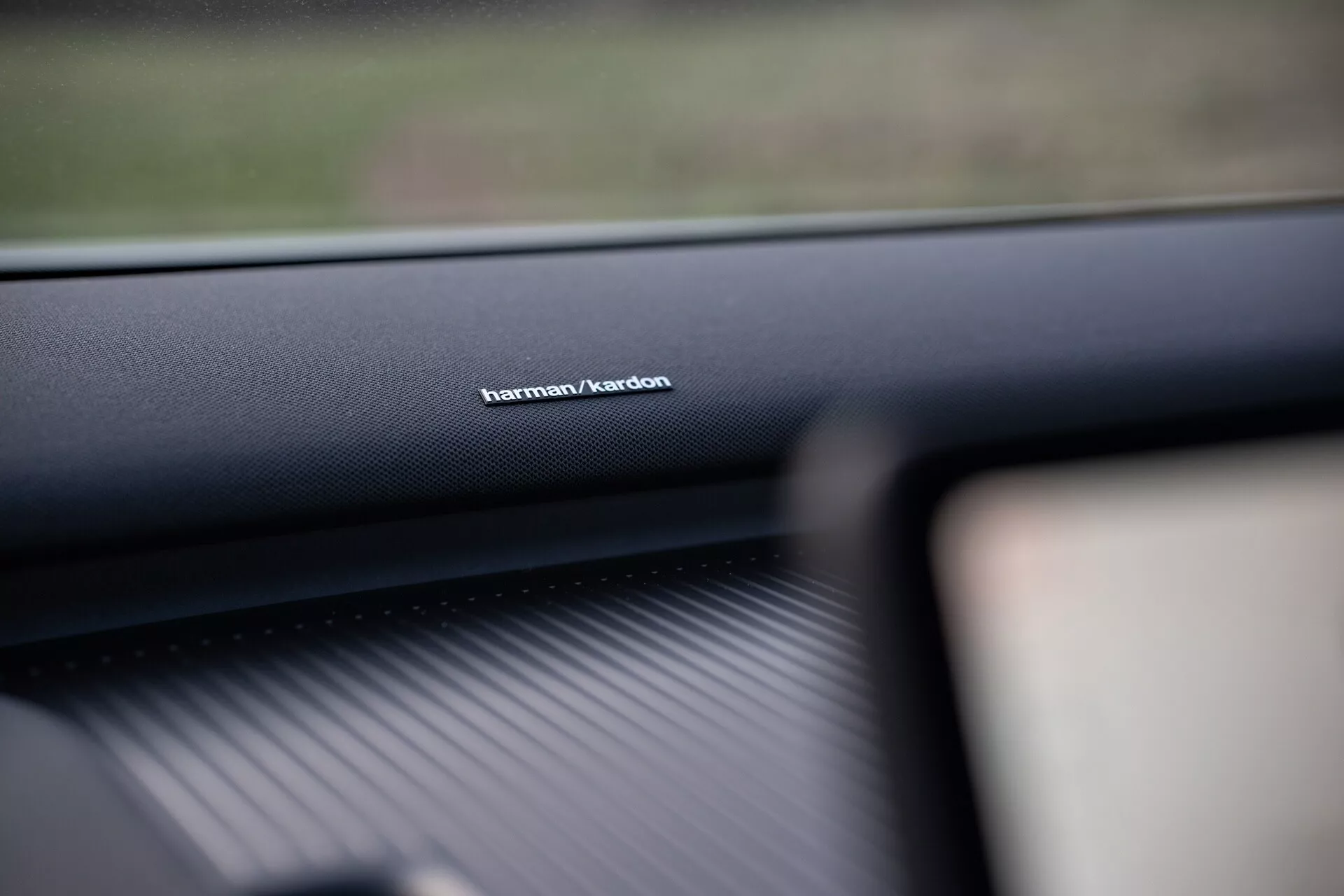Foto interior de um Volvo EX30 2024 focando na marca do sistema de áudio Harman/Kardon no painel do lado do passageiro, mostrando a qualidade de material de alta gama e enfatizando a tecnologia superior do sistema de som.