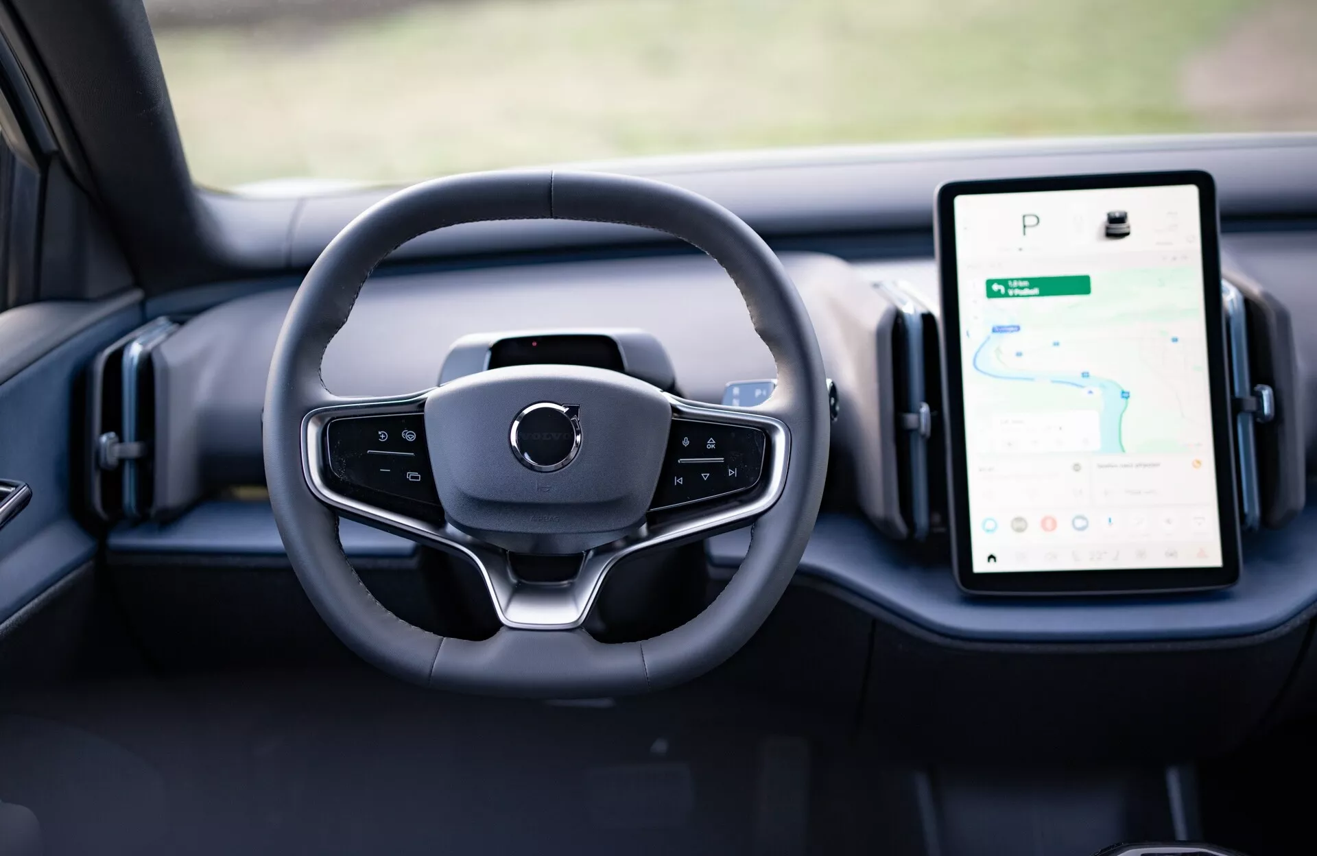 Vista interior do Volvo EX30 2024 mostrando design moderno do volante e mostradores digitais no painel de instrumentos, incluindo o sistema de infotenimento com tela sensível ao toque na vertical com GPS.