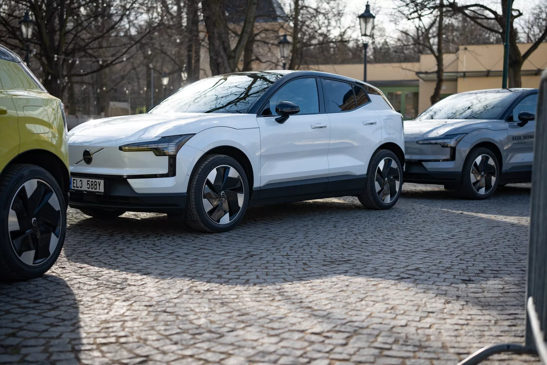 SUV crossover moderno branco de 2024 em vista de três quartos estacionado em uma rua de paralelepípedos, com pintura brilhante, luzes diurnas LED, maçanetas de porta alinhadas à carroceria e rodas de liga leve de design dinâmico sugerindo luxo e performance, provavelmente um veículo elétrico.