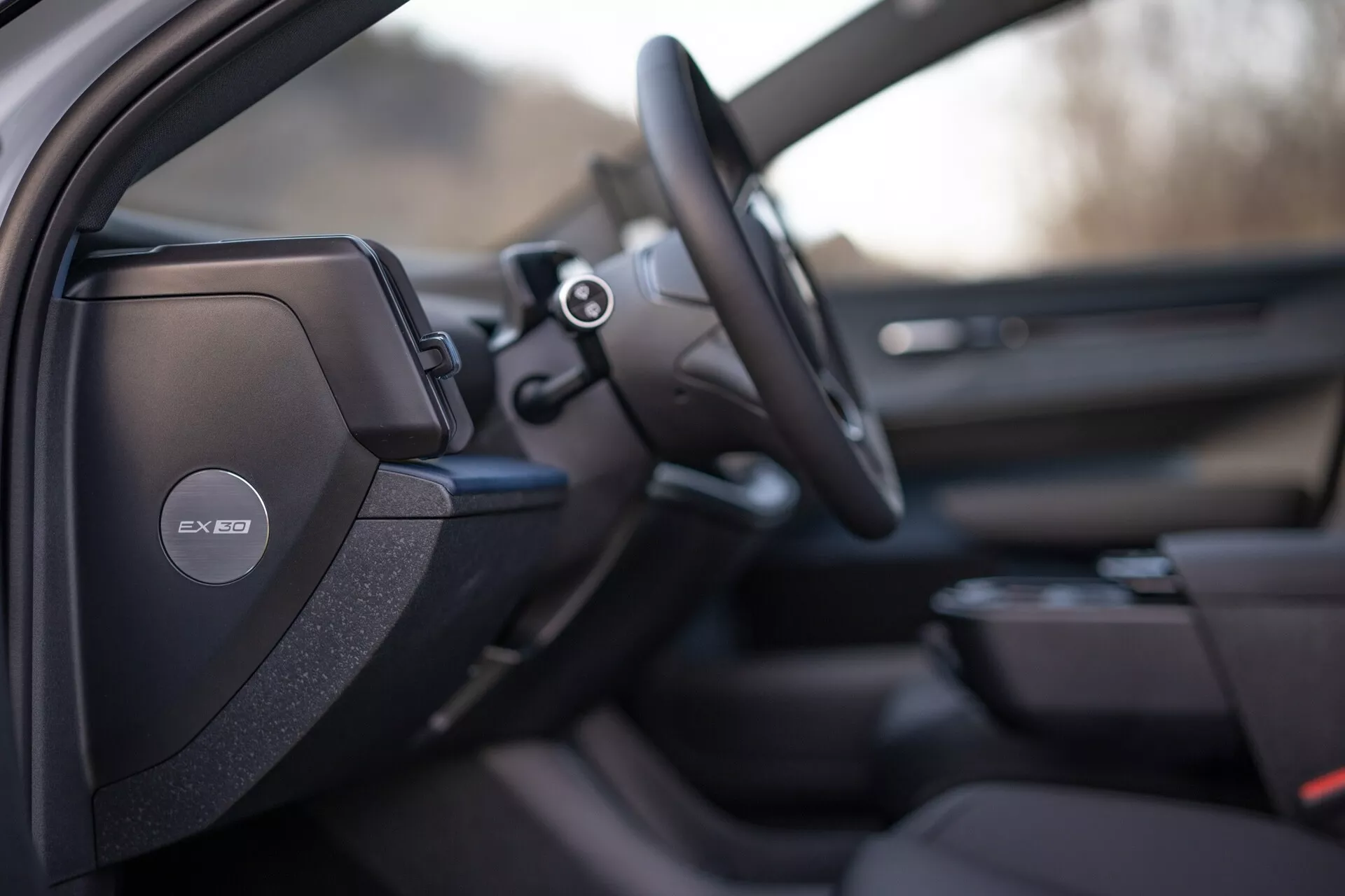 Vista interior do Volvo EX30 2024 focada no lado do motorista com design de assento desportivo ou premium detalhado, sistema de áudio Harman Kardon no pilar B, volante multifuncional e dicas de sistema de infotainment avançado e design do painel da porta do passageiro