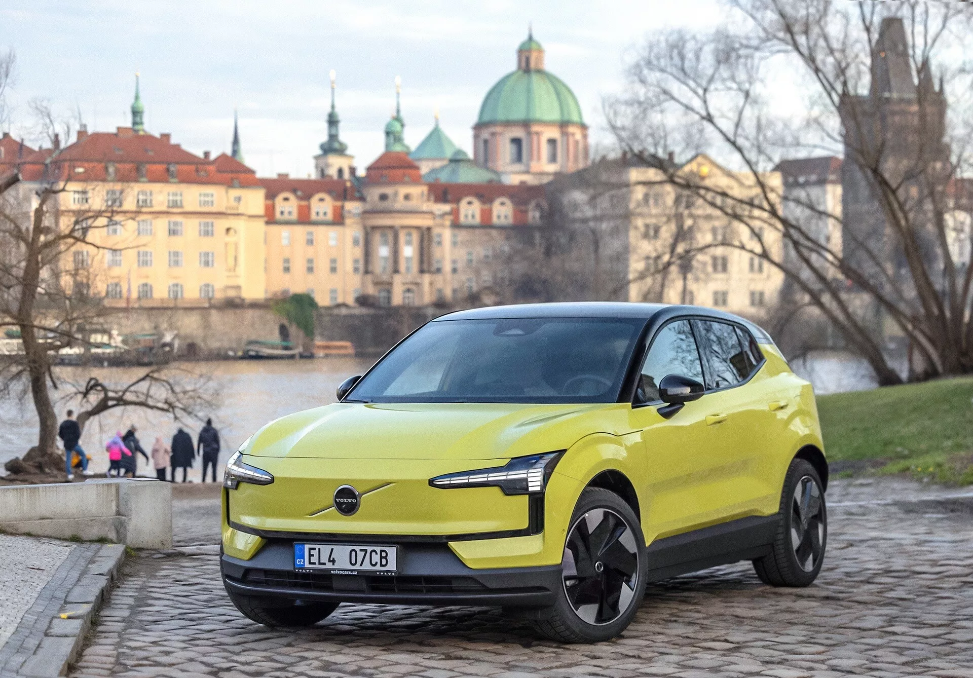 Volvo EX30 2024 em verde lima, vista frontal de três quartos sobre calçada, com faróis LED modernos e características de design elétrico, fundo urbano europeu