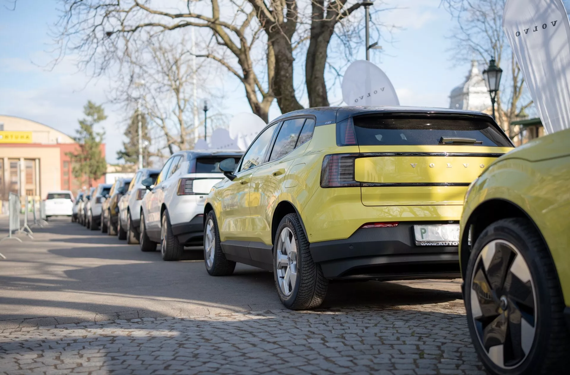 Volvo EX30 de 2024 em verde-limão, exibindo sua vista traseira com conjunto de luzes traseiras LED e aros de liga de múltiplos raios, estacionado ao longo de uma rua urbana