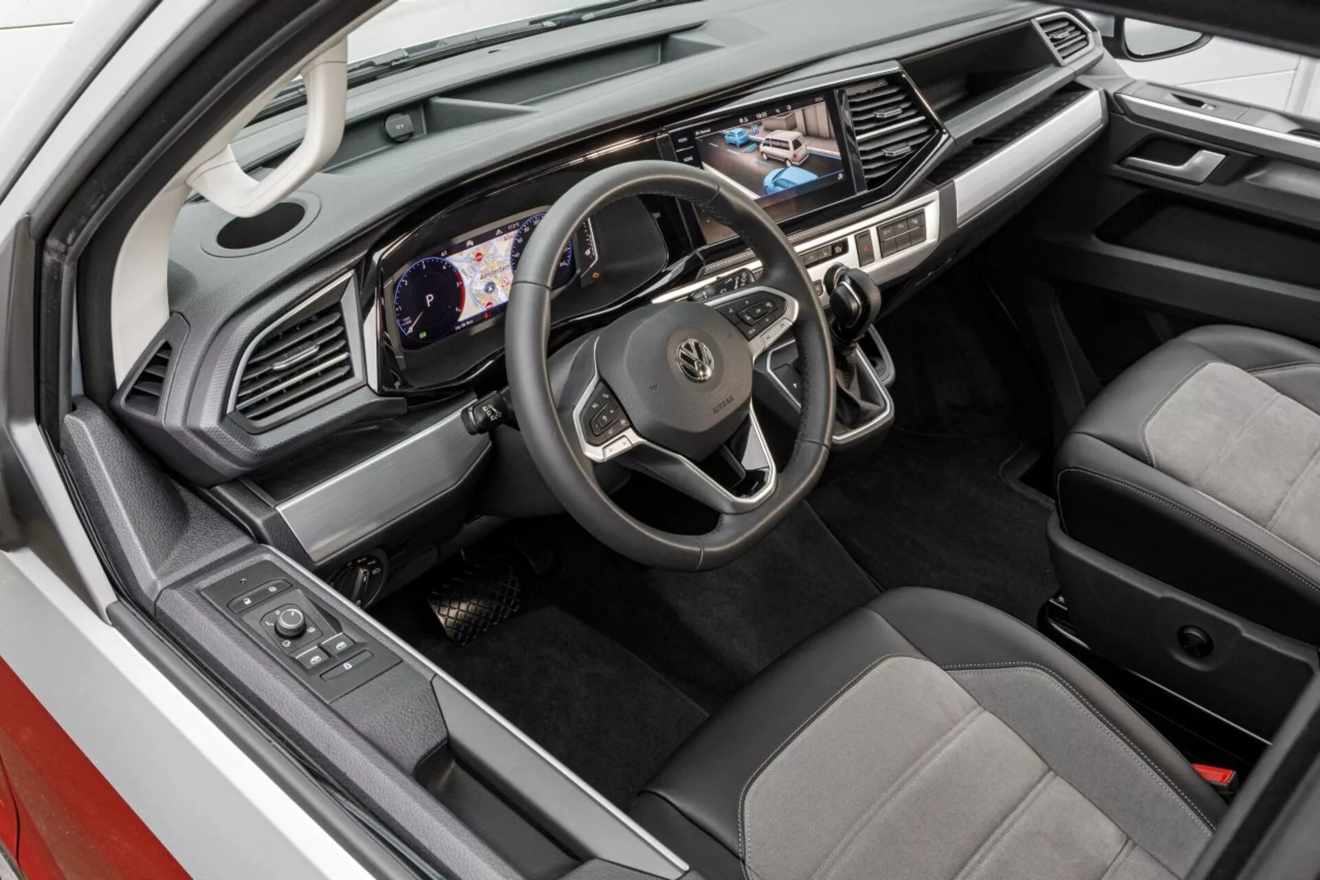 Vista interior de um VW Nutzfahrzeuge Transporter (T6.1 California) 2019 focada no lado do motorista com volante multifuncional, cluster de instrumentos digital, sistema de infoentretenimento e recursos tecnológicos avançados, configuração de condução à direita, em um layout de cabine ergonômico.