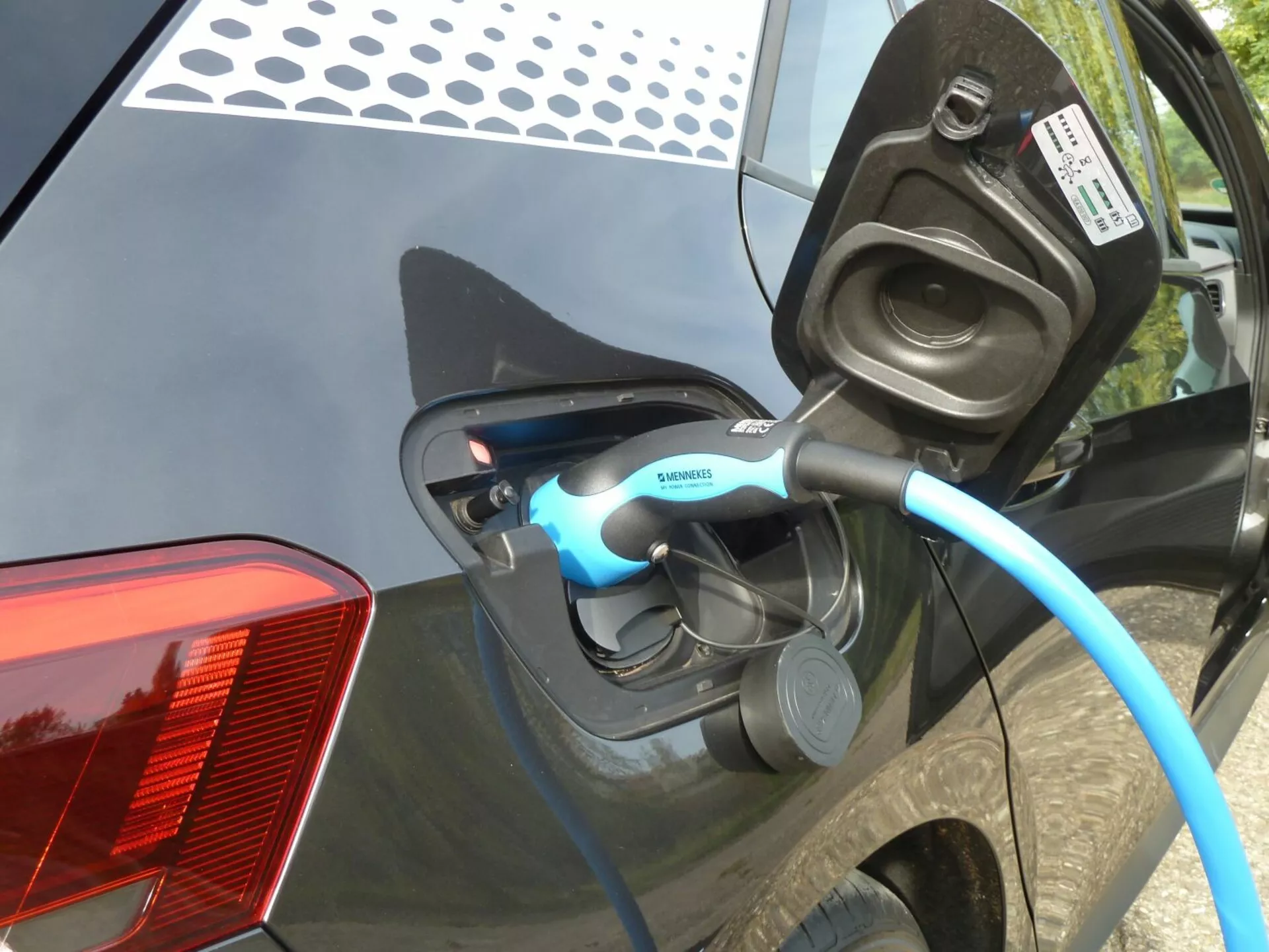 Vista detalhada do carregamento de um veículo elétrico VW ID.3 2020, focando na porta de carregamento aberta e no cabo com marca Siemens na lateral traseira do carro, com indicador LED visível e características detalhadas como o design moderno da luz traseira LED e a carroceria escura e brilhante.