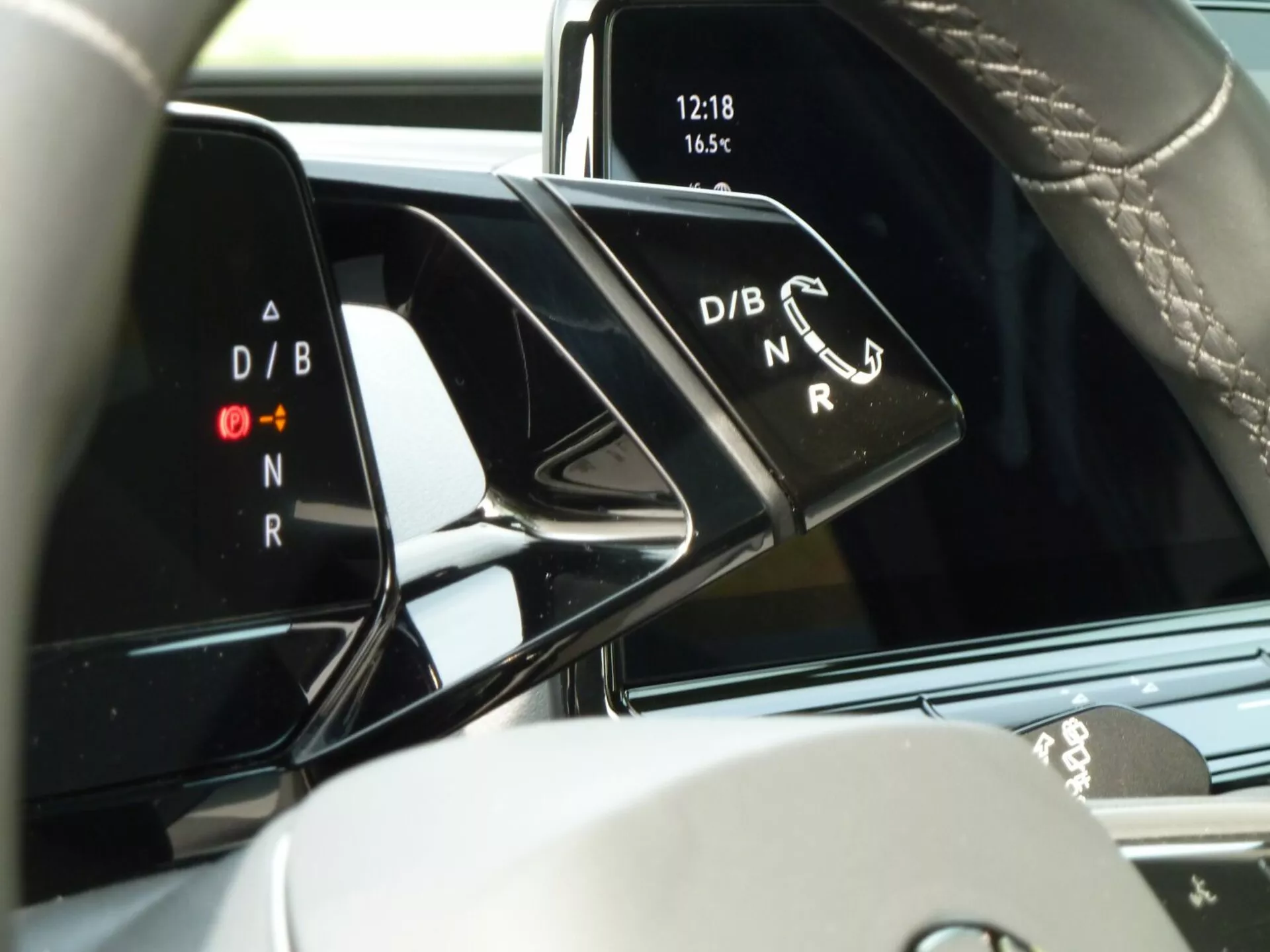 Interior do VW ID.3 2020 em destaque com o console central e um close no seletor de marchas mostrando indicadores de modo de condução D/B e N/R, relógio no display digital às 12:18 e temperatura a 16,5°, enfatizando a tecnologia moderna do veículo e elementos de design premium.