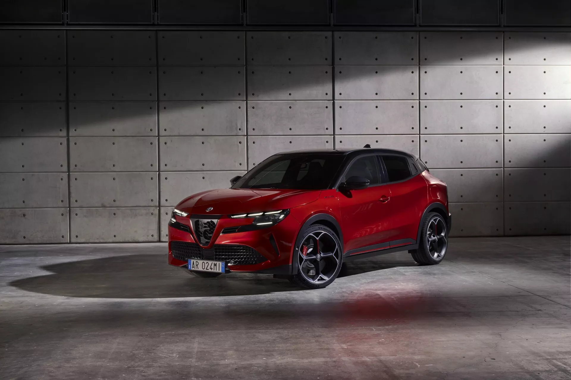 Alfa Romeo Junior 966 de 2024 em vermelho vibrante mostrando design dinâmico e recursos avançados em um cenário de estúdio profissional com fundo industrial