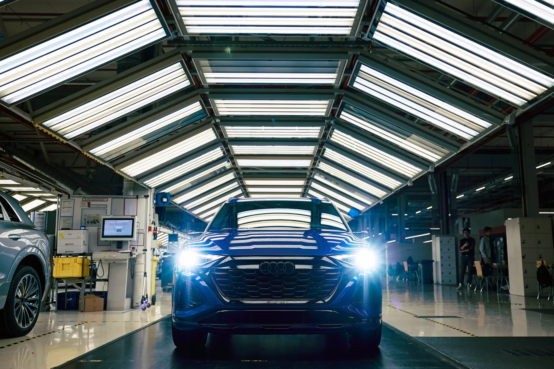 Vista frontal do Audi Q8 e-tron 2023 numa oficina com piso refletor, destacando sua grade horizontal e faróis LED.