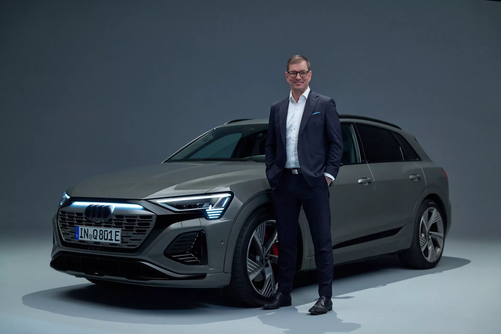 Audi Q8 e-tron 2023 em ambiente de estúdio, apresentando grade frontal, faróis LED, rodas de liga leve multiraiadas e estilo de carroceria SUV elegante com homem em traje de negócios para escala