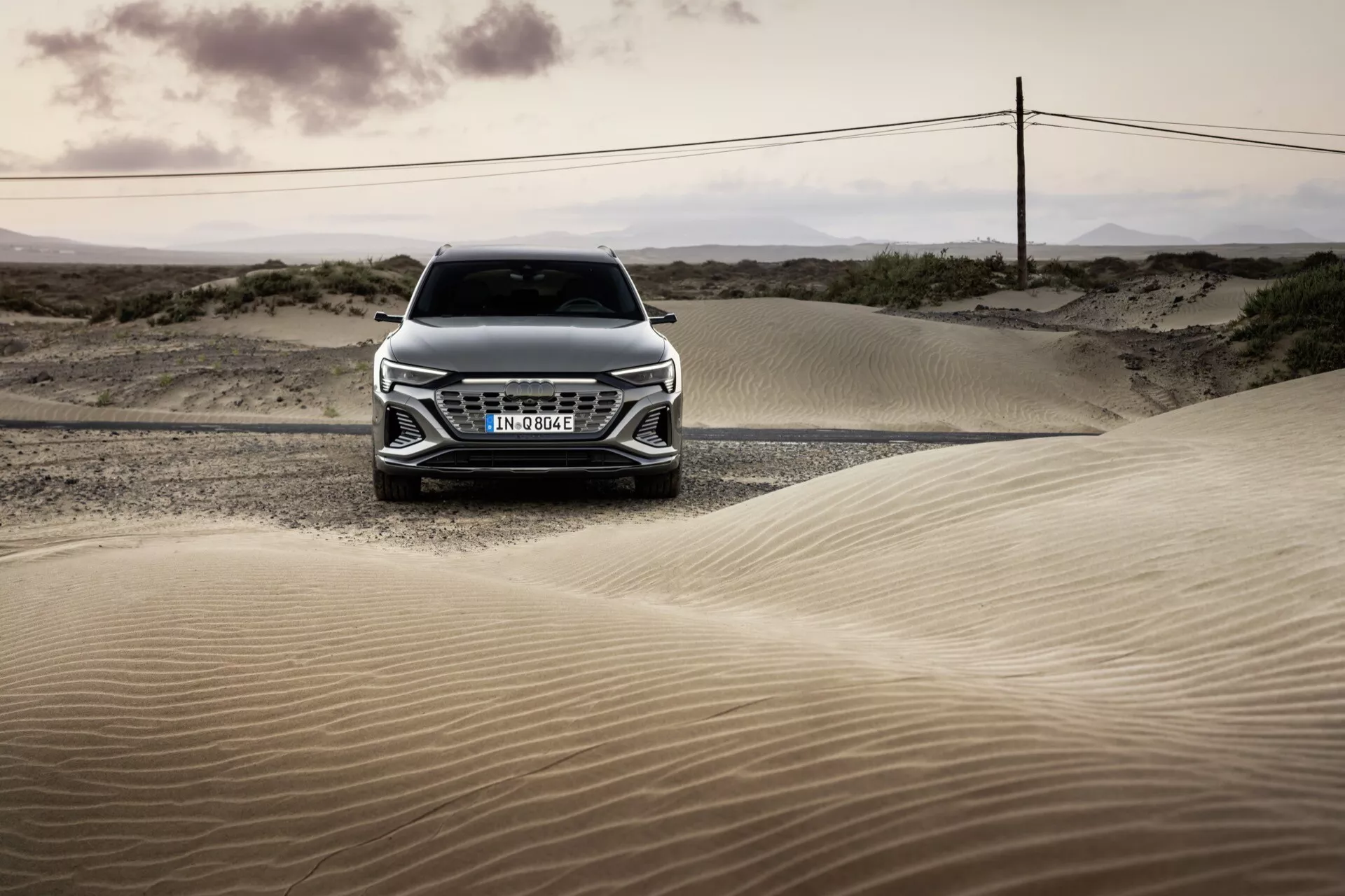 Vista frontal do Audi Q8 e-tron 2023 em uma paisagem desértica ao amanhecer ou anoitecer, destacando sua grade, capô e design avançado de faróis