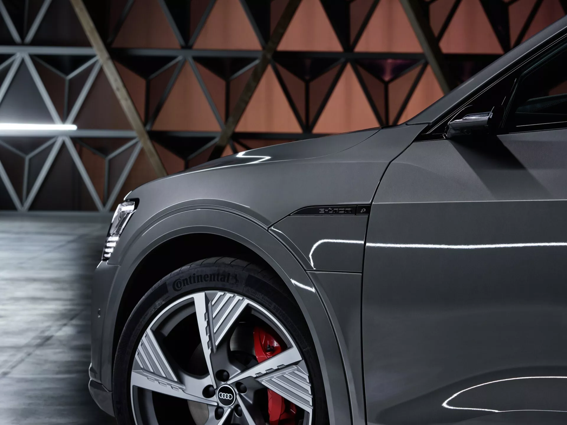 Vista lateral em close-up do Audi Q8 e-tron 2023 focando no painel frontal do quarto, exibindo roda de liga leve multirraios, pneu de alta performance Continental, pinça de freio vermelha com grande disco, e pintura brilhante com linhas de design esportivo