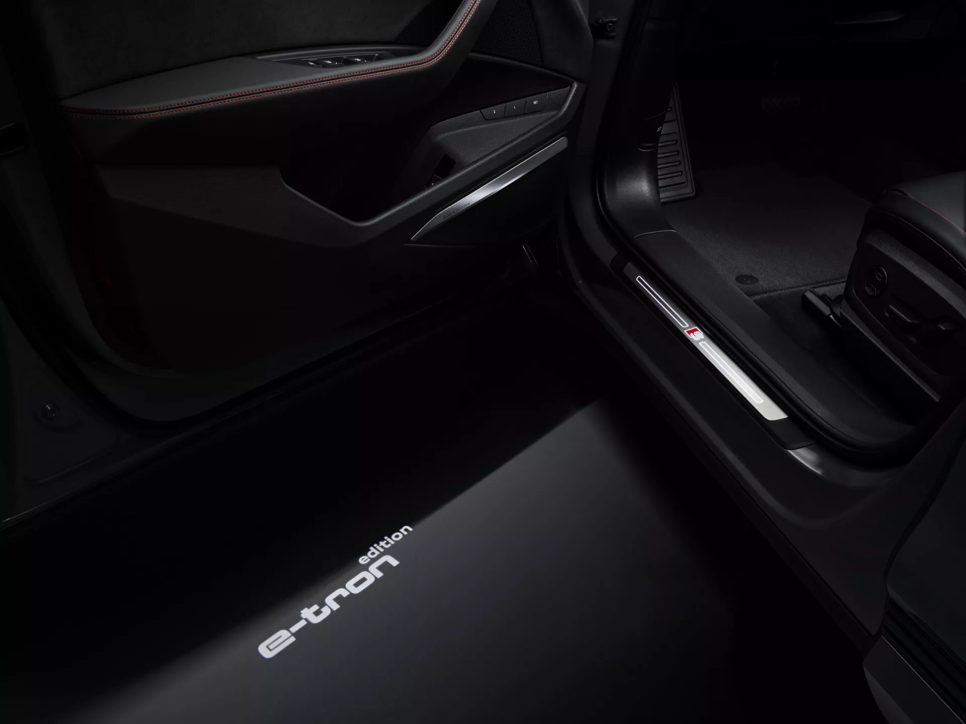 Visão de ângulo baixo da soleira da porta do lado do passageiro interior do Audi Q8 e-tron 2023 exibindo a inscrição iluminada 'e-tron', iluminação interior aprimorada e detalhes de acabamento premium